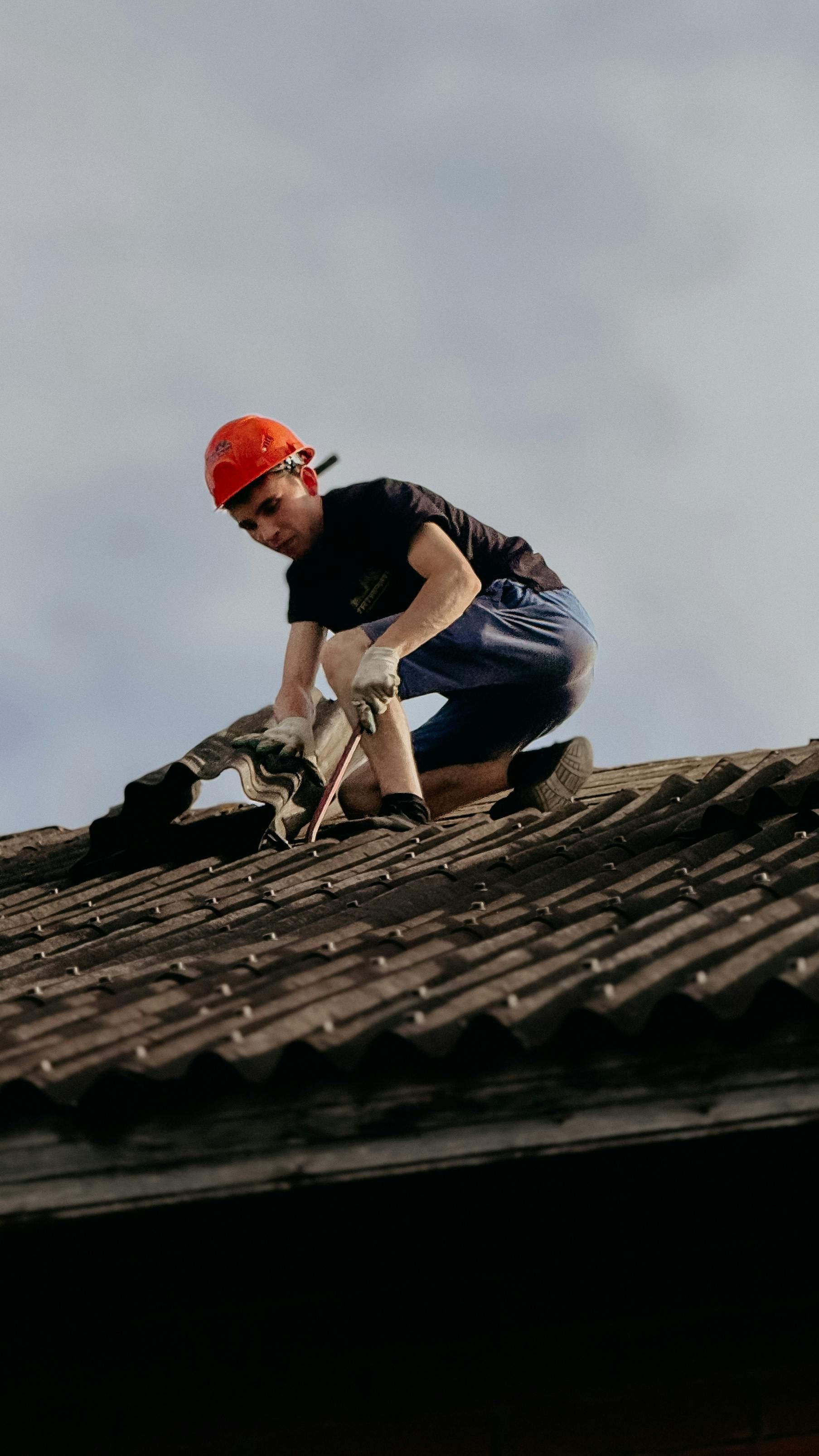 Worker in orange hard hat repairing a roof under a cloudy sky