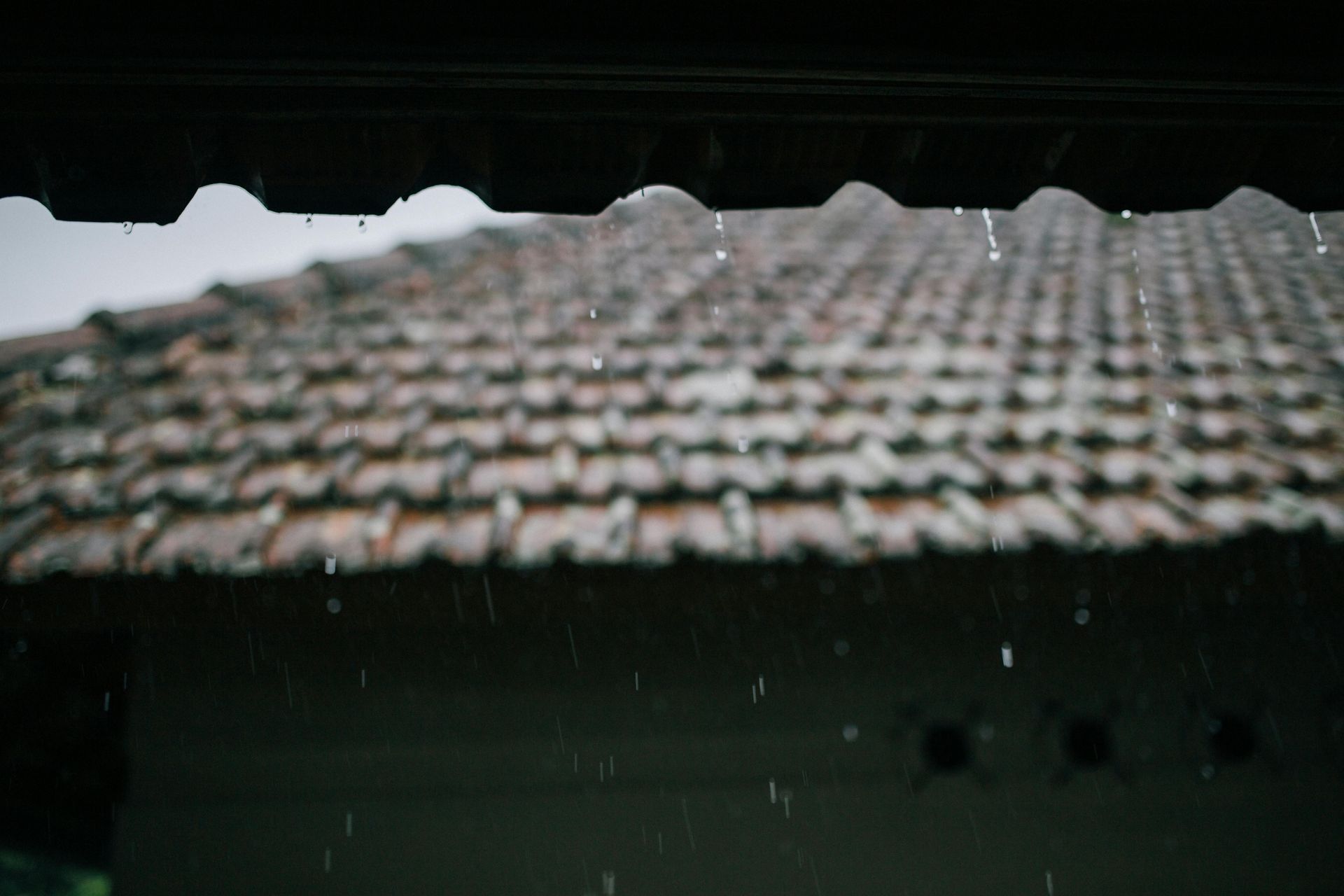 Rain falling on a tiled roof seen through a dark window frame