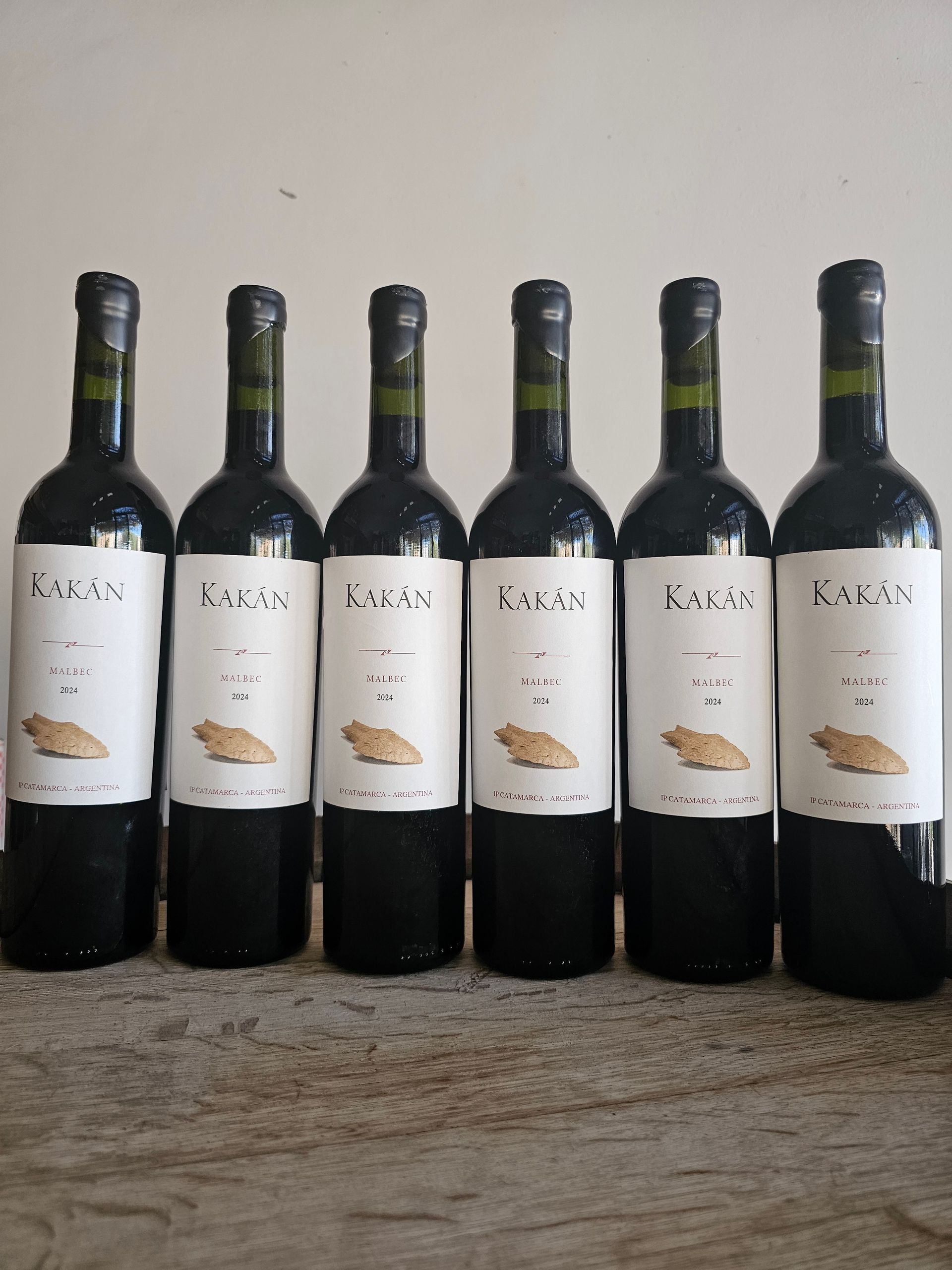 Seis botellas de vino tinto con etiquetas blancas sobre una superficie de madera.