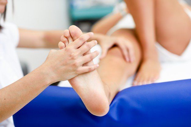 Persona recibiendo masaje de pies, con terapeuta sosteniendo el pie sobre una mesa azul.