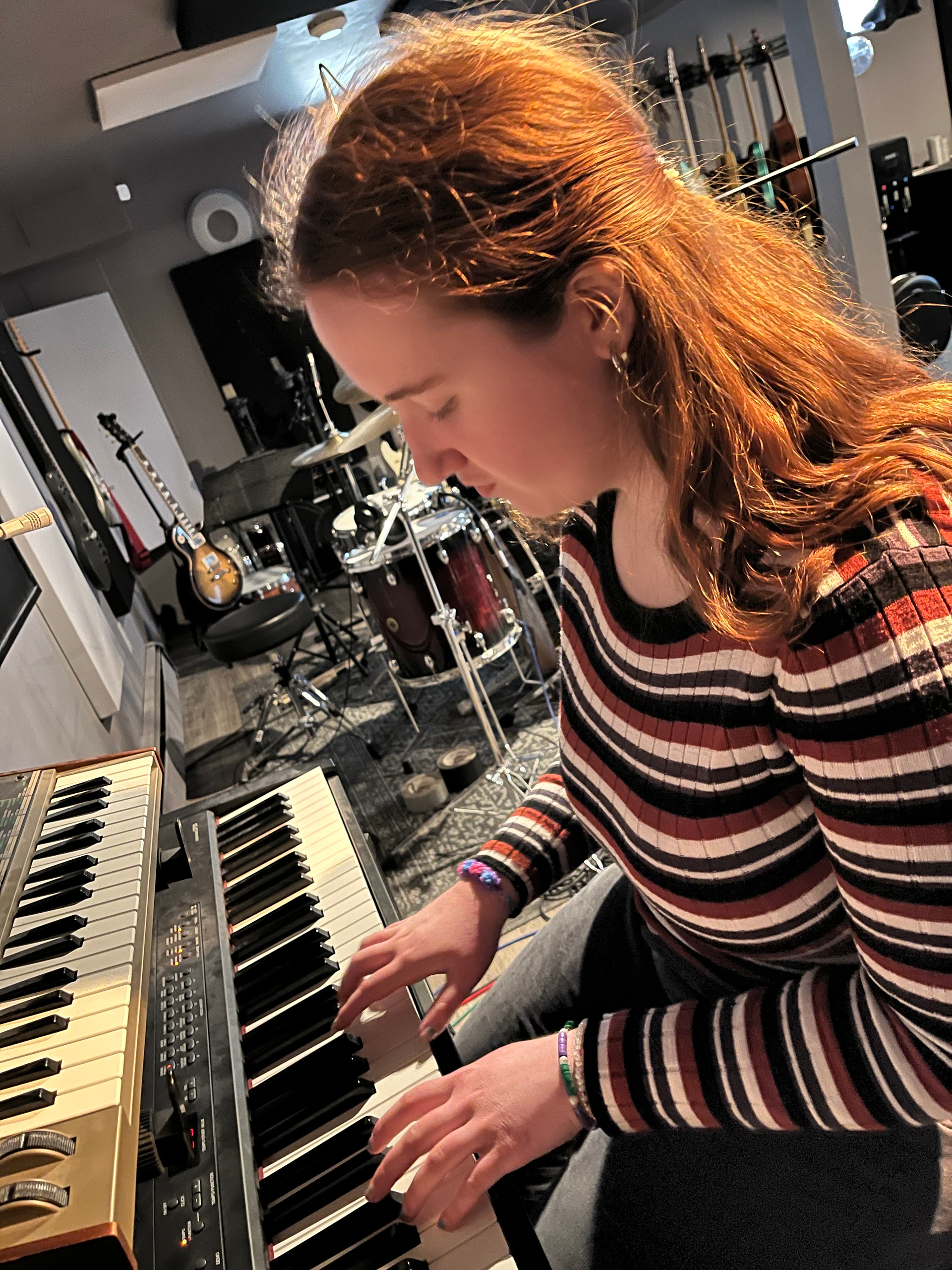 A woman is playing a keyboard in a room with drums in the background.