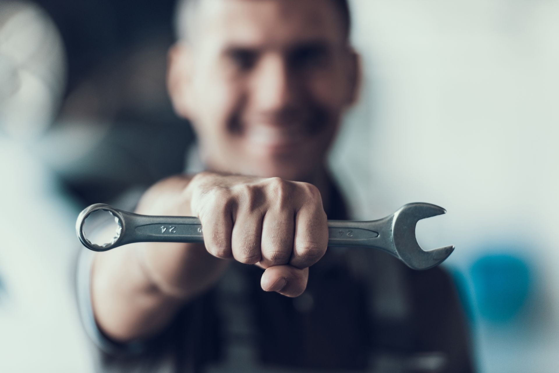 Il meccanico solleva una chiave inglese, sorridendo. Contesto di un'officina automobilistica, concentrato sullo strumento.