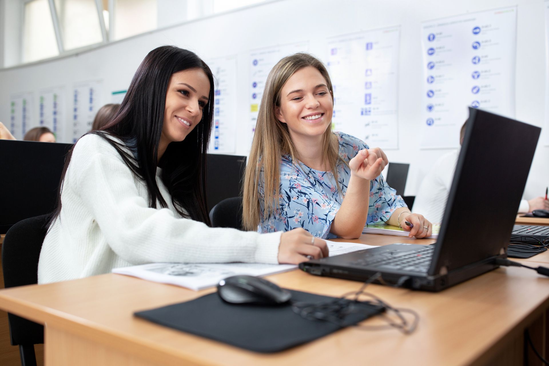Due donne sorridono davanti allo schermo di un computer portatile in un'aula.
