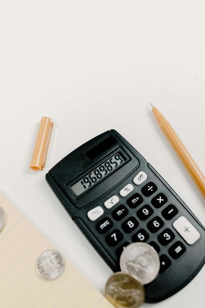 Calculator on a white desk with coins and pencils nearby