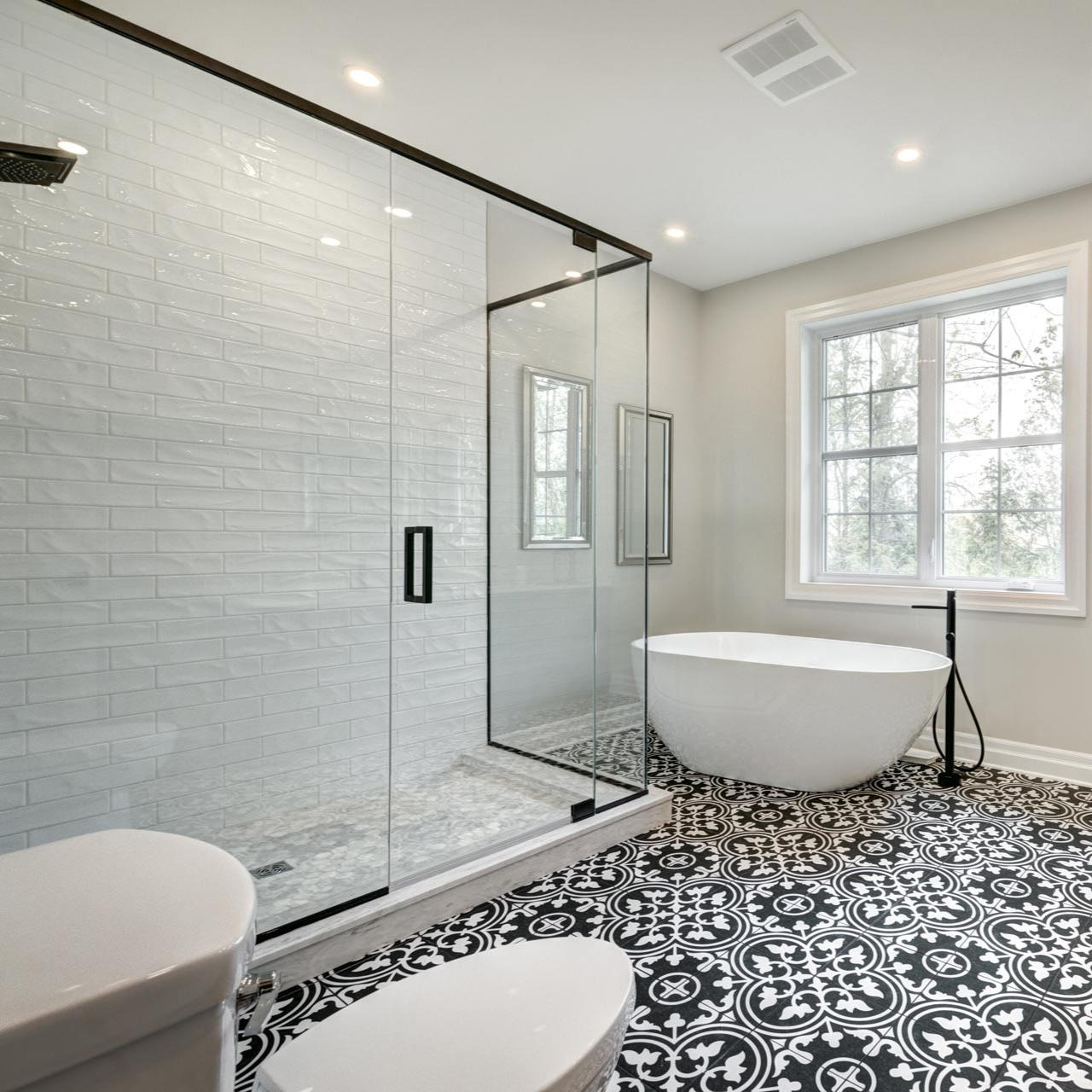 Modern bathroom with glass shower, freestanding tub, and black-and-white patterned floor by a window