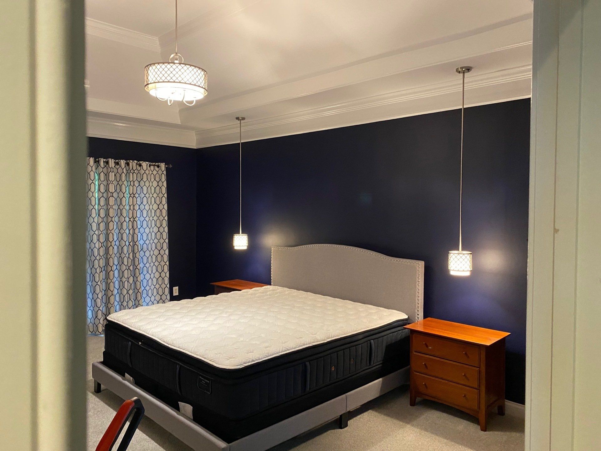 Bedroom with dark blue walls, a bed, hanging pendant lights, and a wooden nightstand.