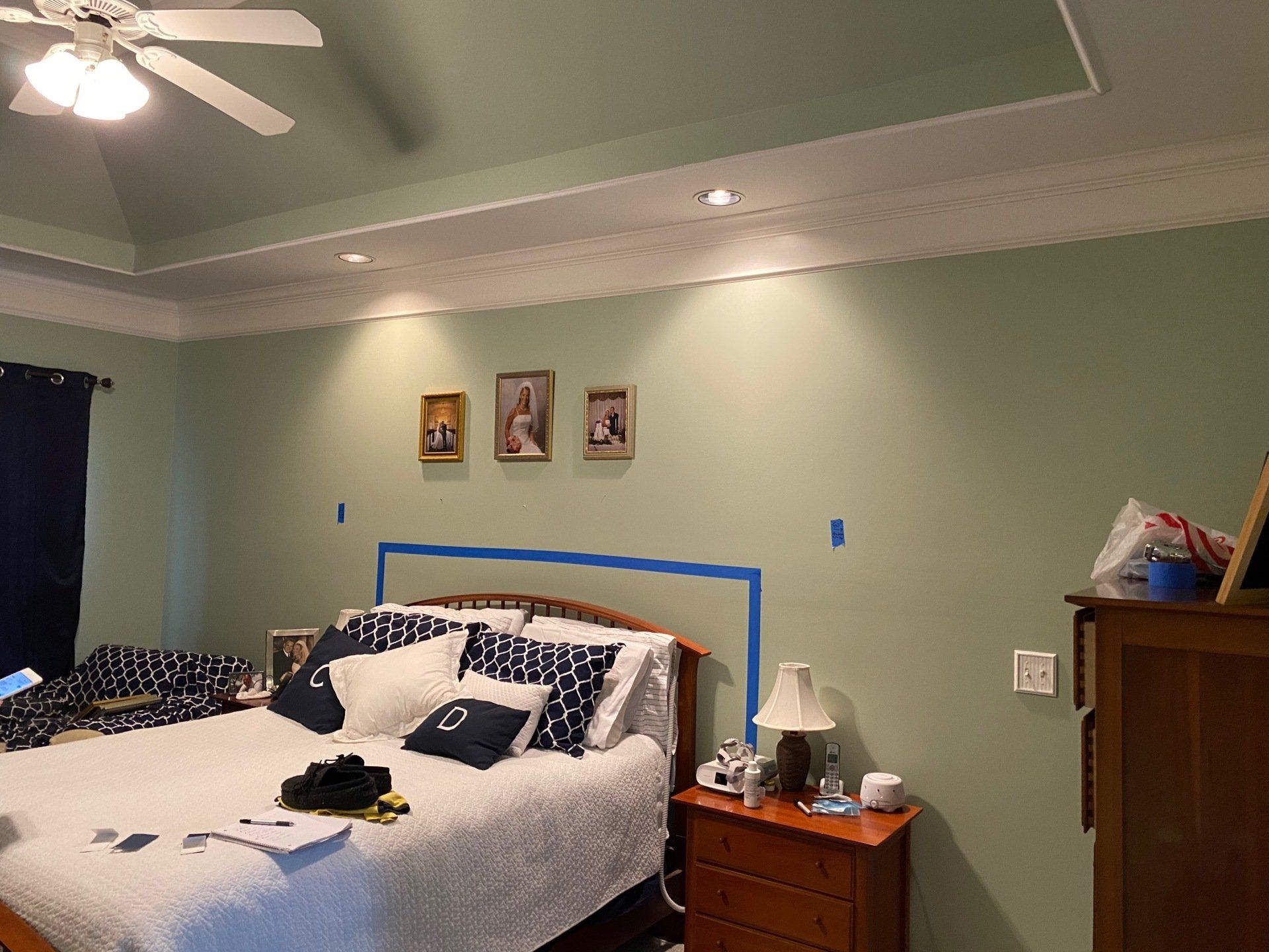 Bedroom with a bed, dresser, lamp, green walls, and framed photos above the headboard.