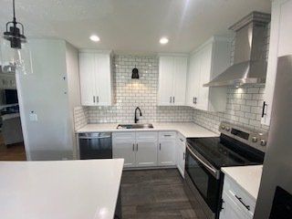 Bright white kitchen with gray tile backsplash, stainless appliances, and dark wood flooring