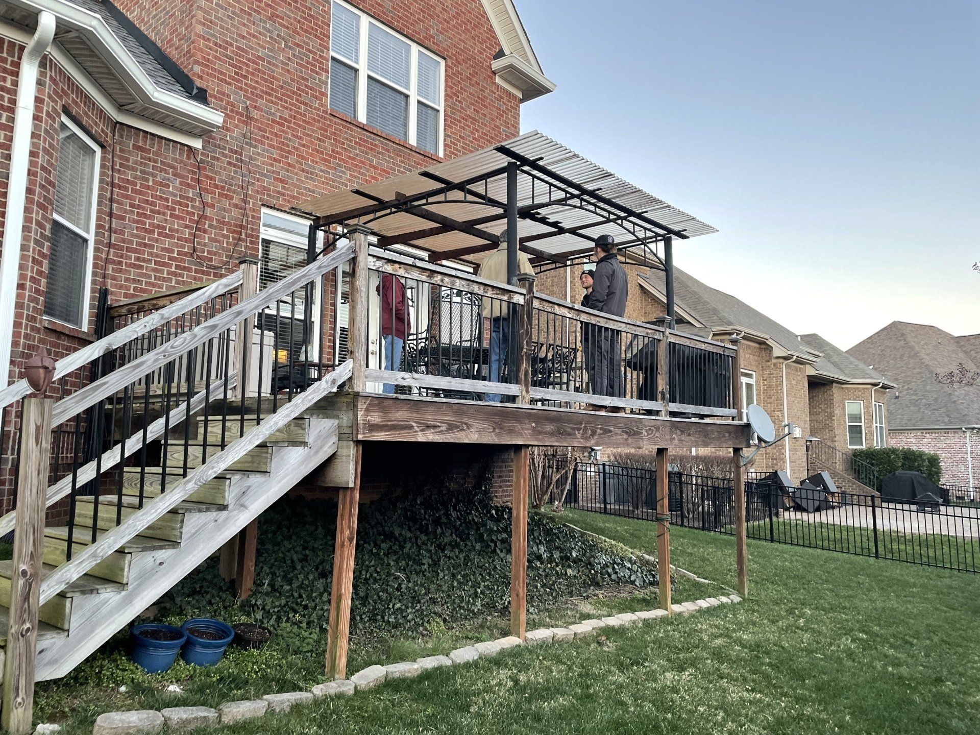 Back deck under construction on a brick house, with stairs, railings, and a pergola frame