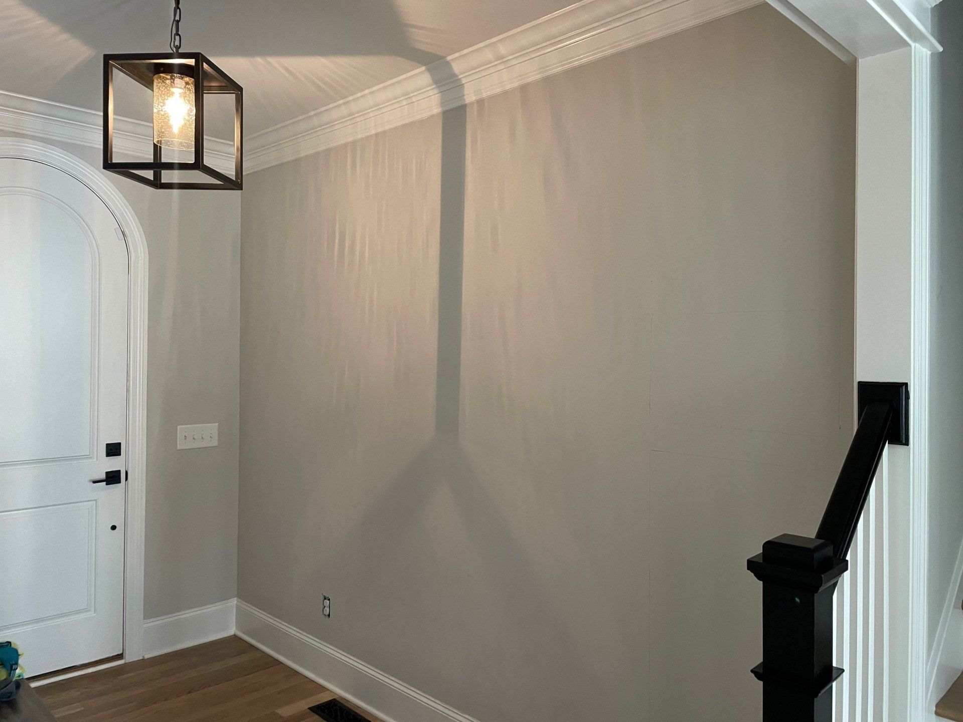Empty hallway with gray walls, white door, and a black hanging light fixture casting shadows.