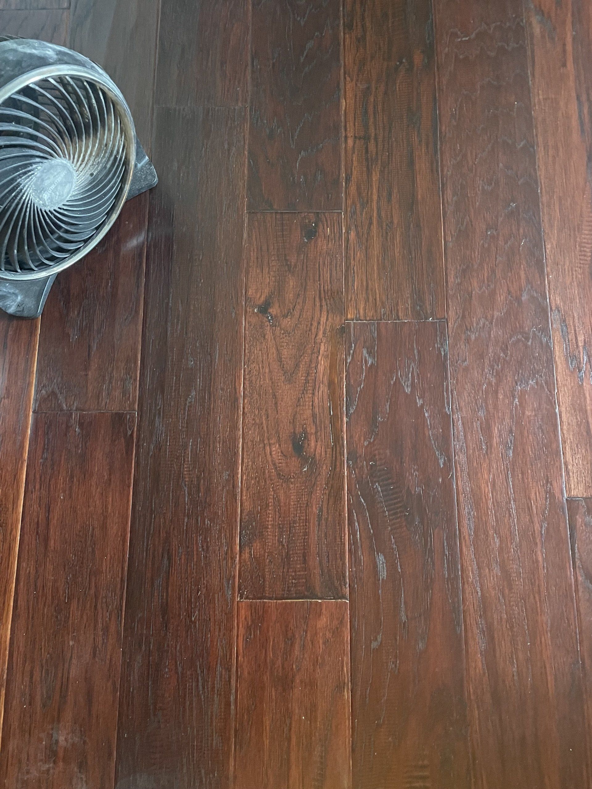 Dark wooden floor with a black fan or appliance partially visible in the top left corner