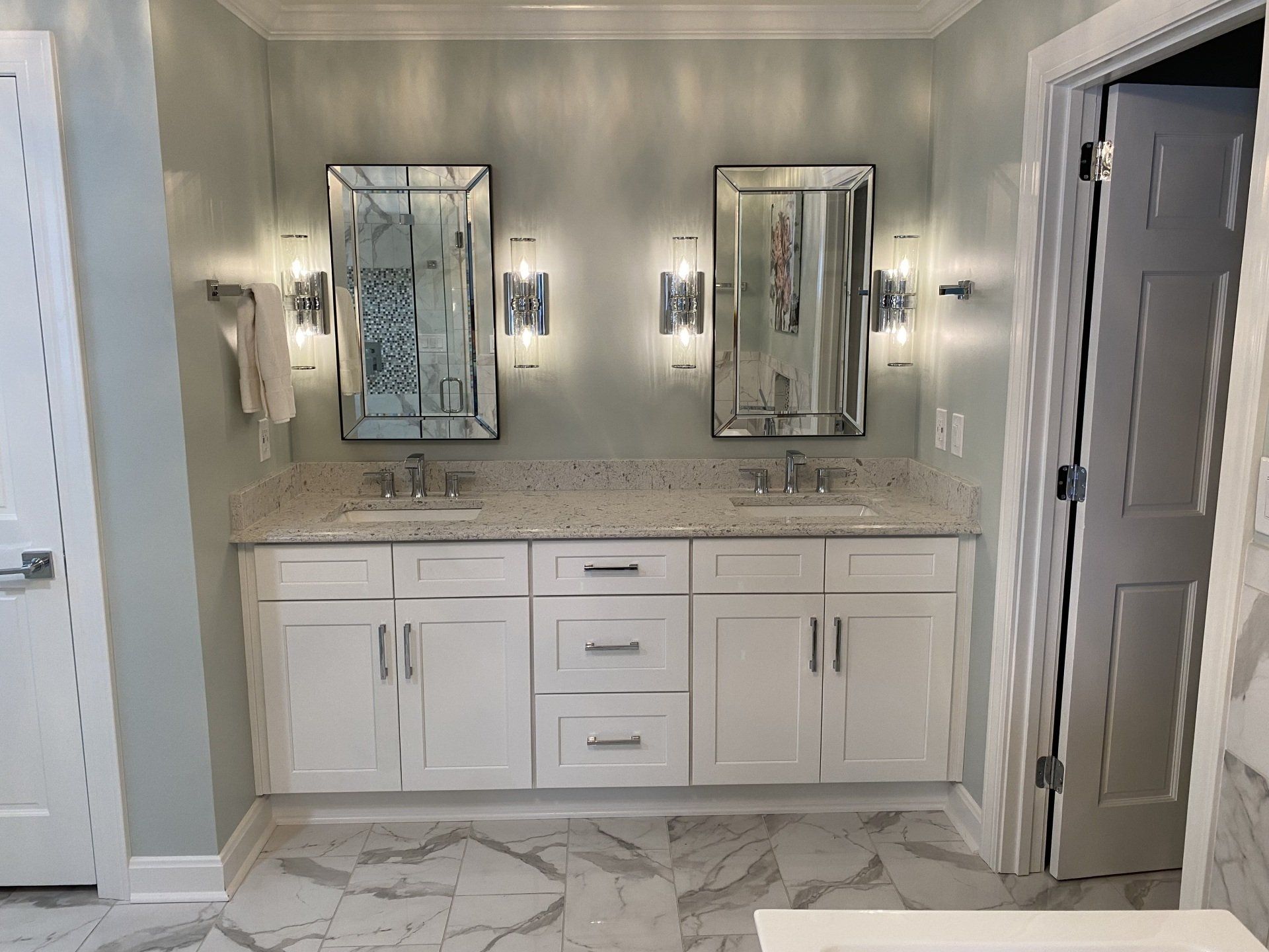 Bathroom vanity with white cabinets, marble countertop, two mirrors, and wall sconces under soft lighting
