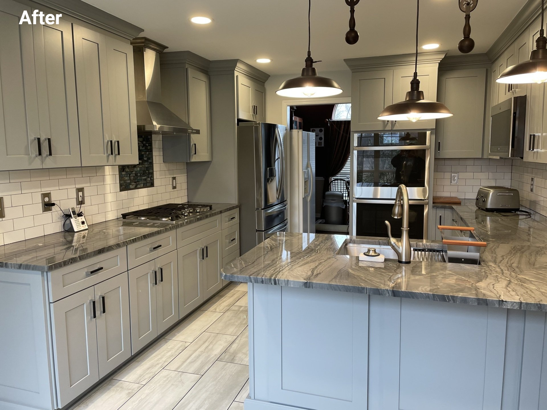 Modern gray kitchen with island, pendant lights, marble counters, and stainless steel appliances