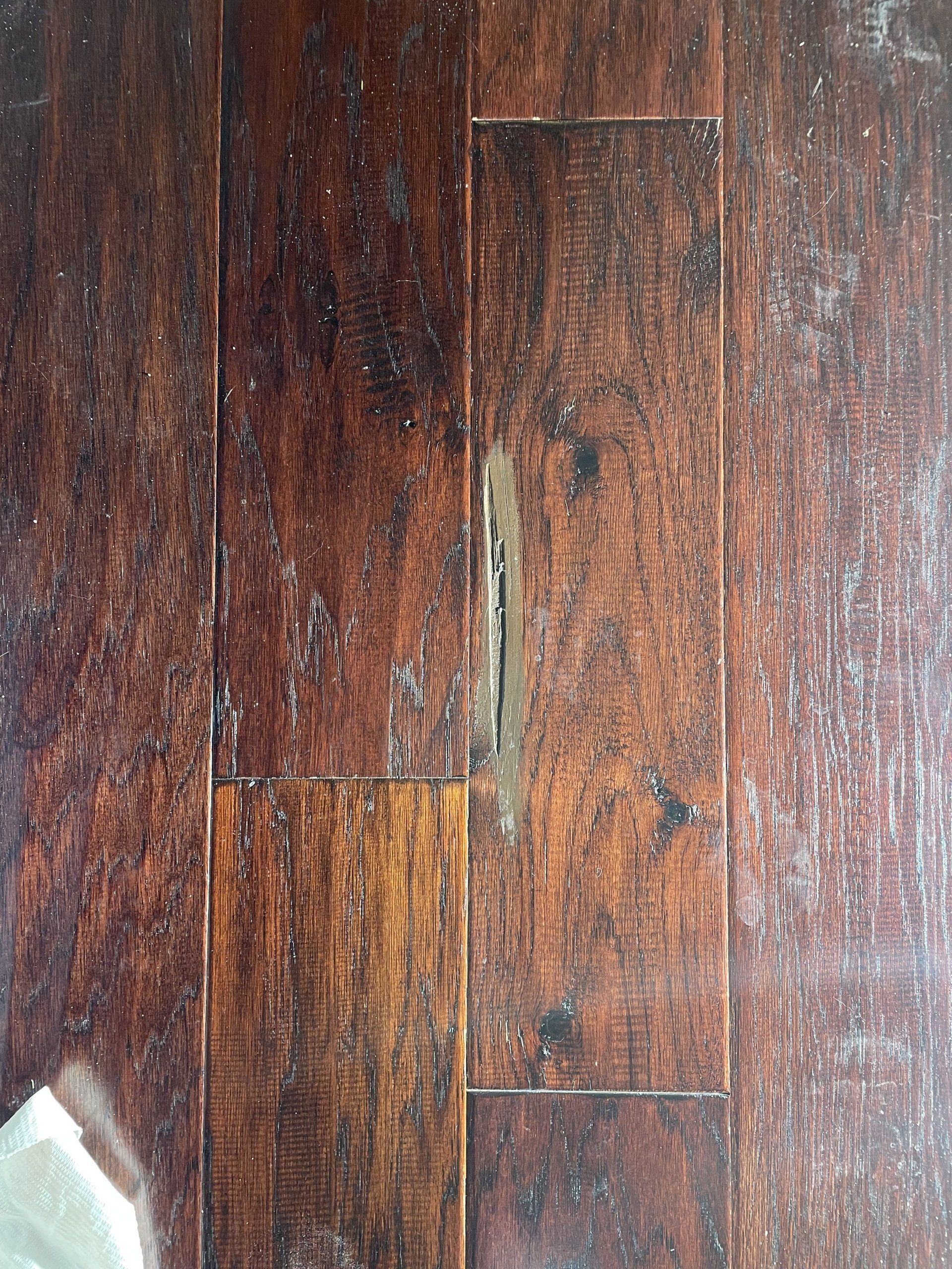 Close-up of a scratched, weathered dark wood floor with a small white corner visible