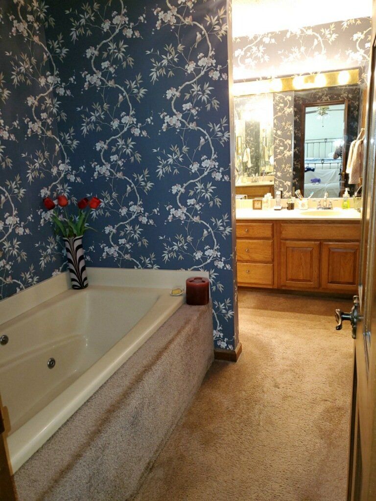 Bathroom with blue floral wallpaper, a white tub, and a vanity with mirror lights.