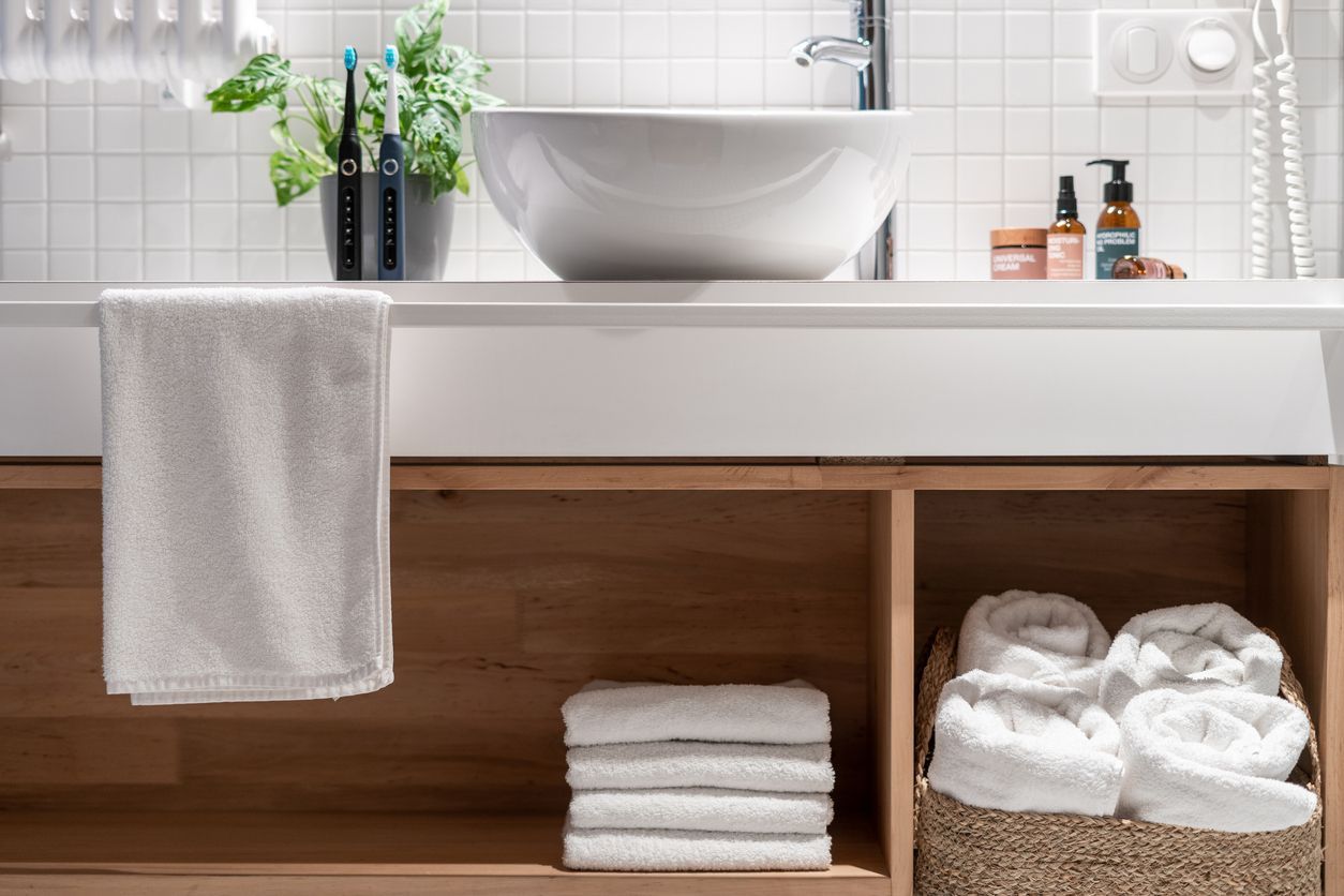 Modern bathroom vanity with white vessel sink, towel, and neatly stacked towels under the counter