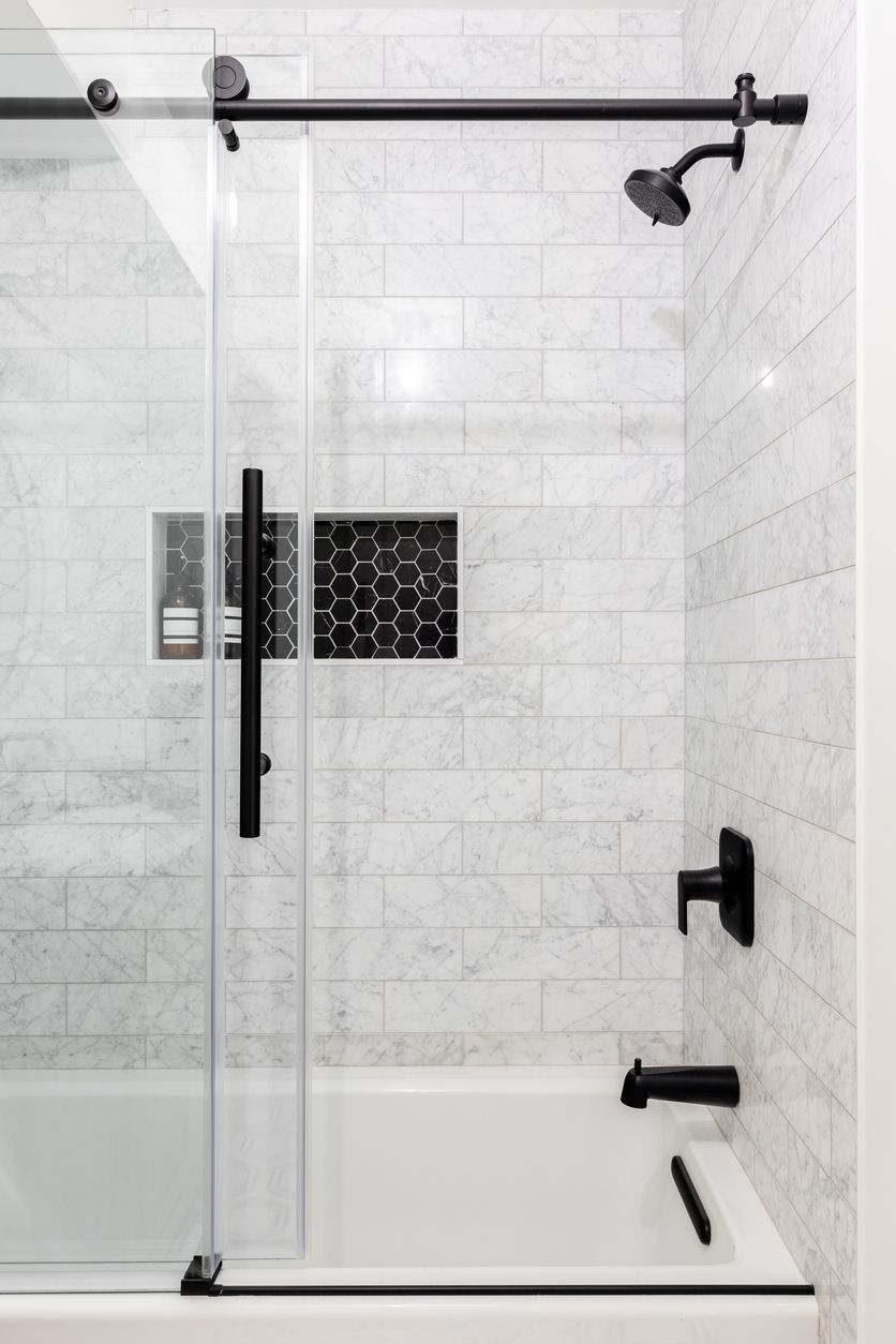 Modern tiled shower with sliding glass door and black grab bars