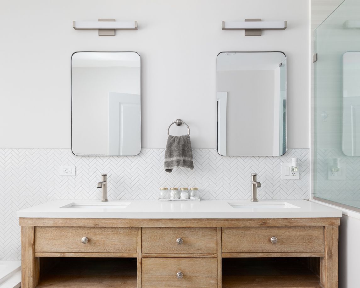 Modern bathroom vanity with two mirrors, twin sinks, and a light wood cabinet underneath.