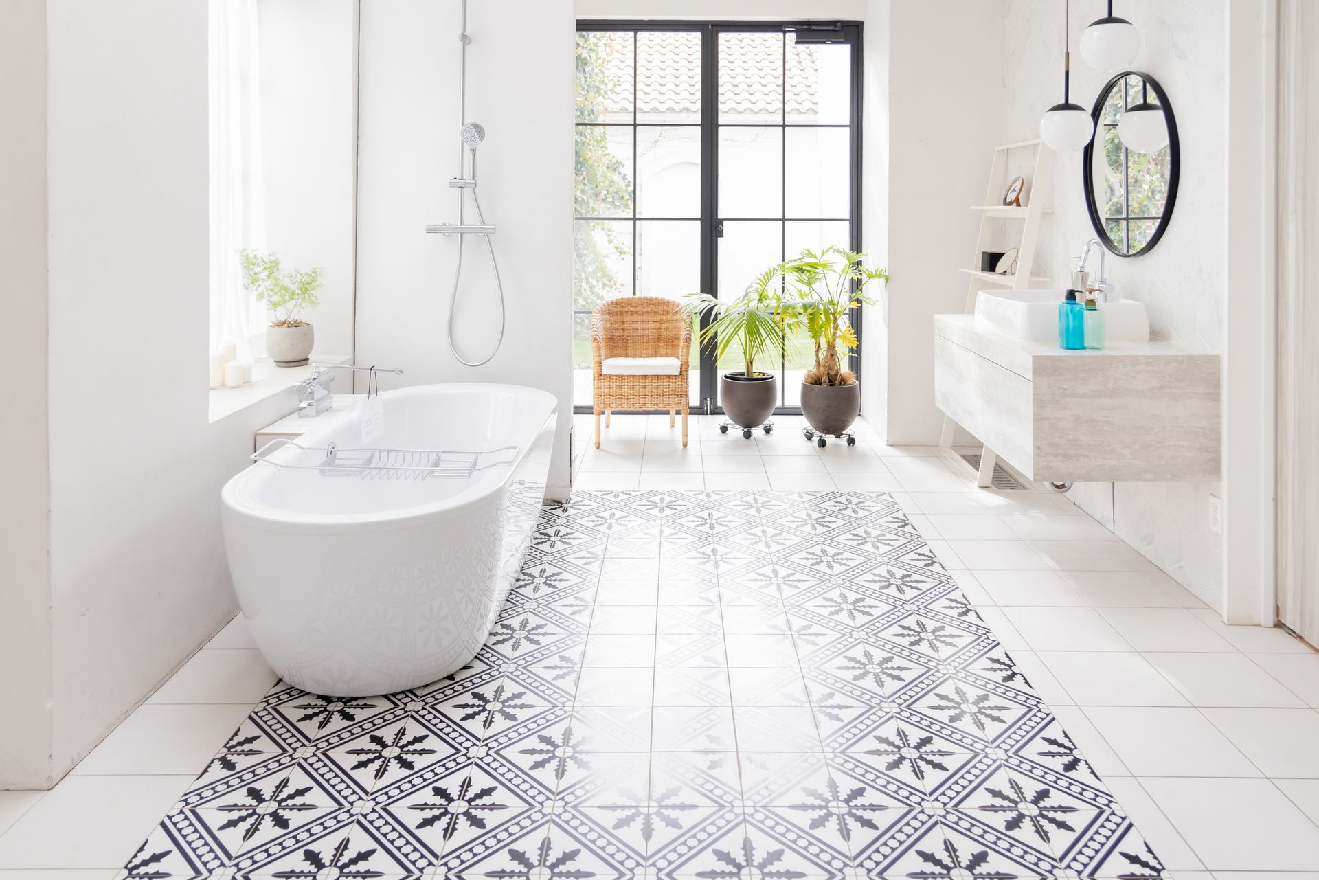 Bright modern bathroom with a freestanding tub, patterned floor, and large window beside a small chair.
