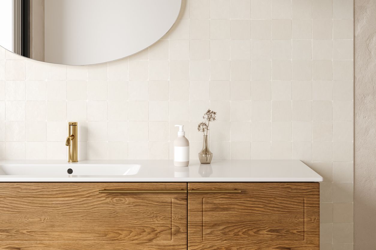 Minimalist bathroom vanity with wood cabinets, white countertop, gold faucet, and round mirror