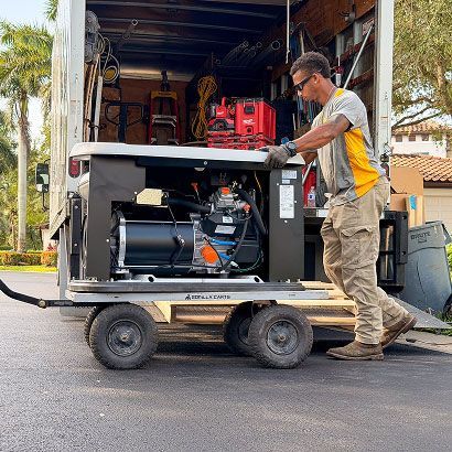 Worker pushing a portable generator on a wheeled cart outside a truck