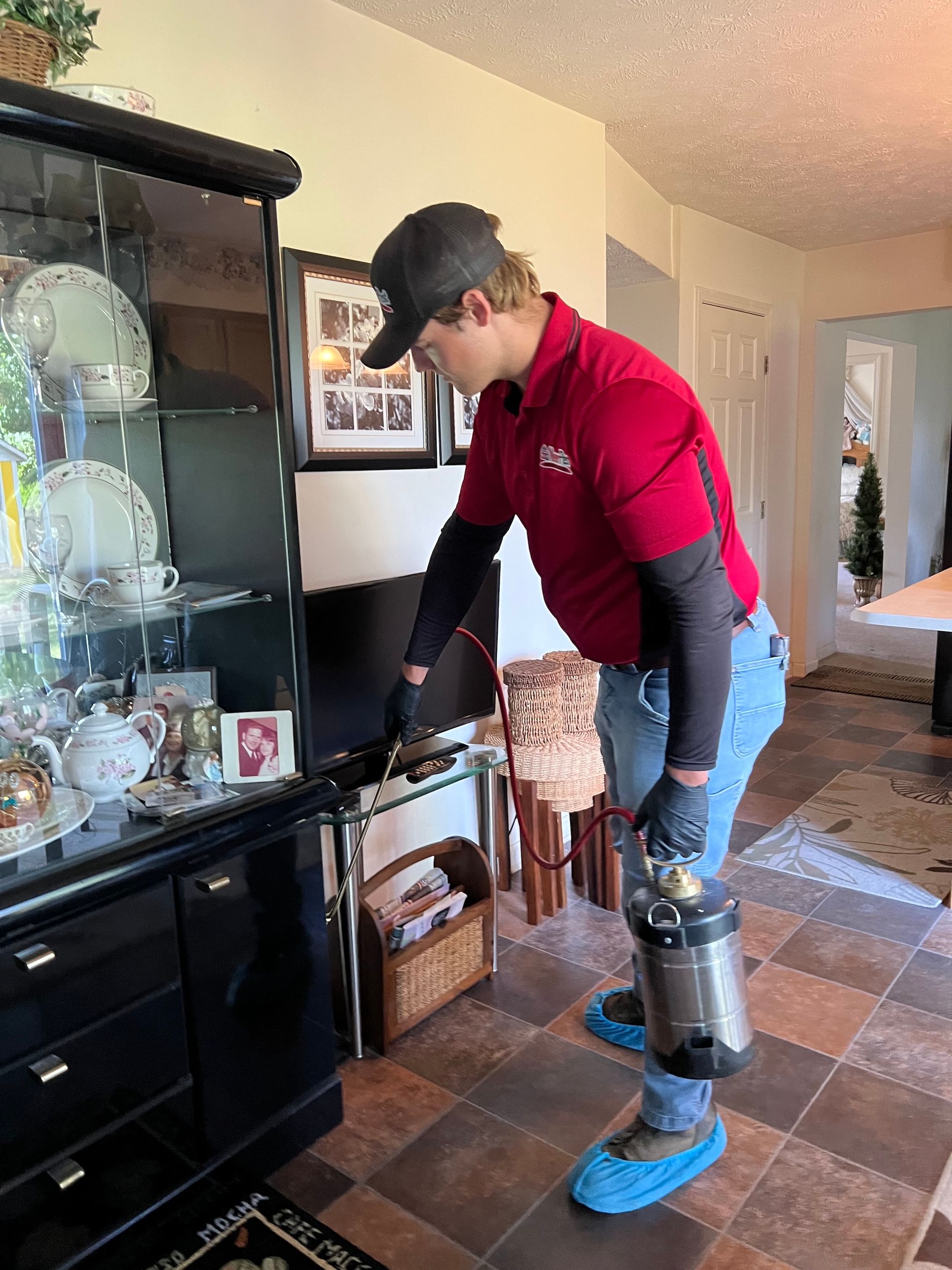 Person in a red shirt and blue shoe covers adjusting a black cabinet in a home dining room.