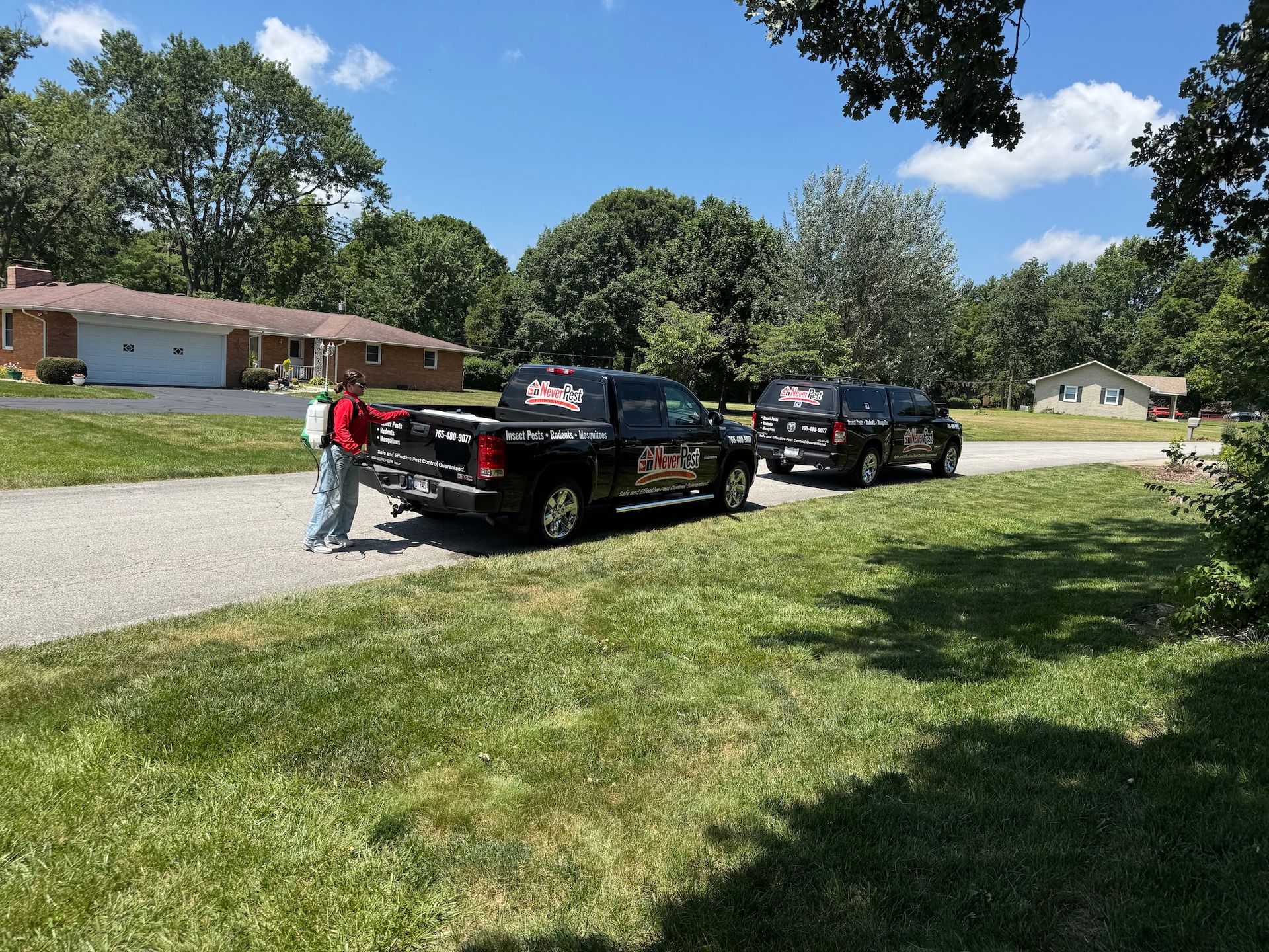 Two black pickup trucks on a suburban street, with a person standing by the rear truck on a sunny day.