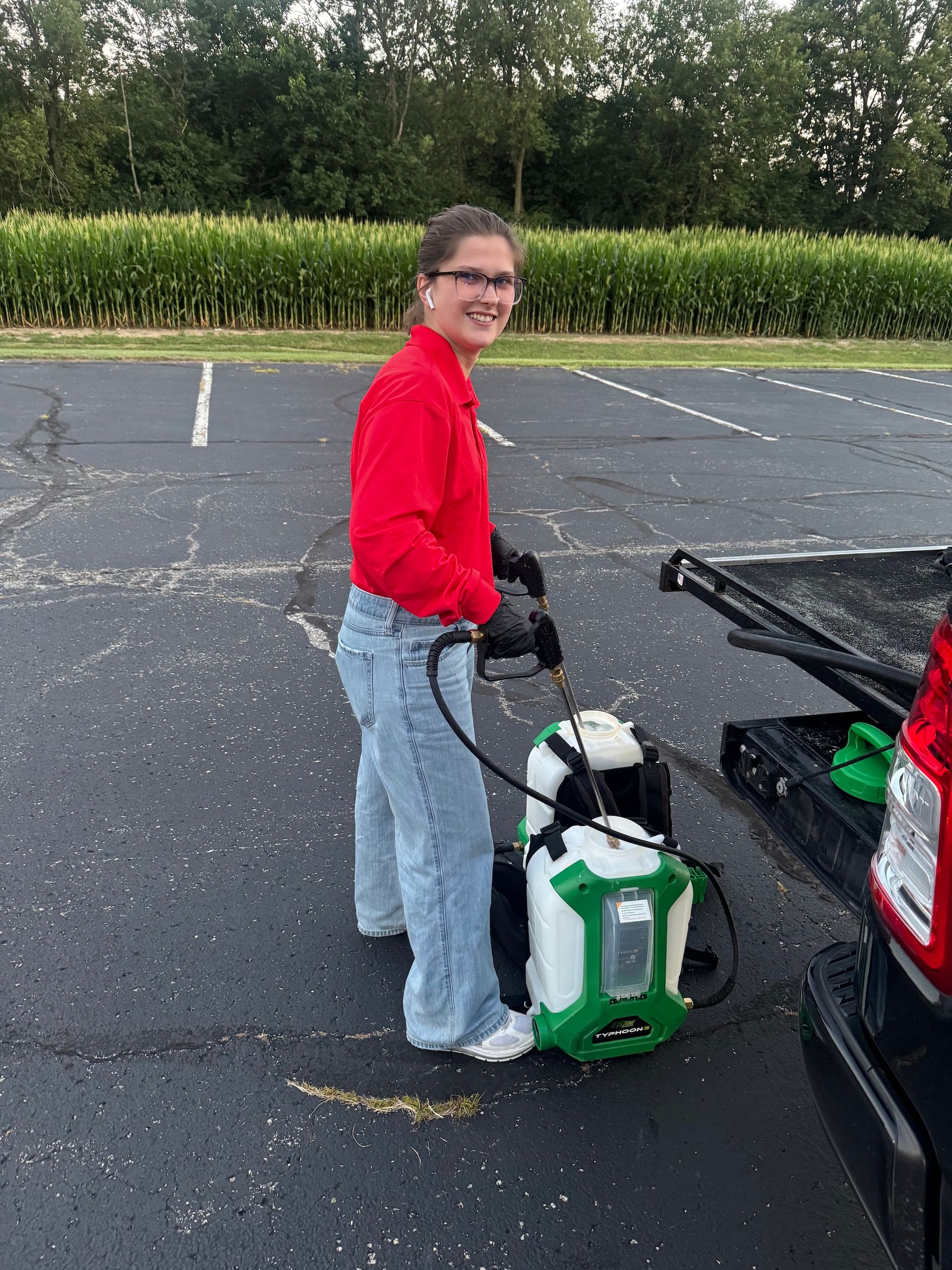 Person in red top loading a green cooler into a car trunk in a parking lot.