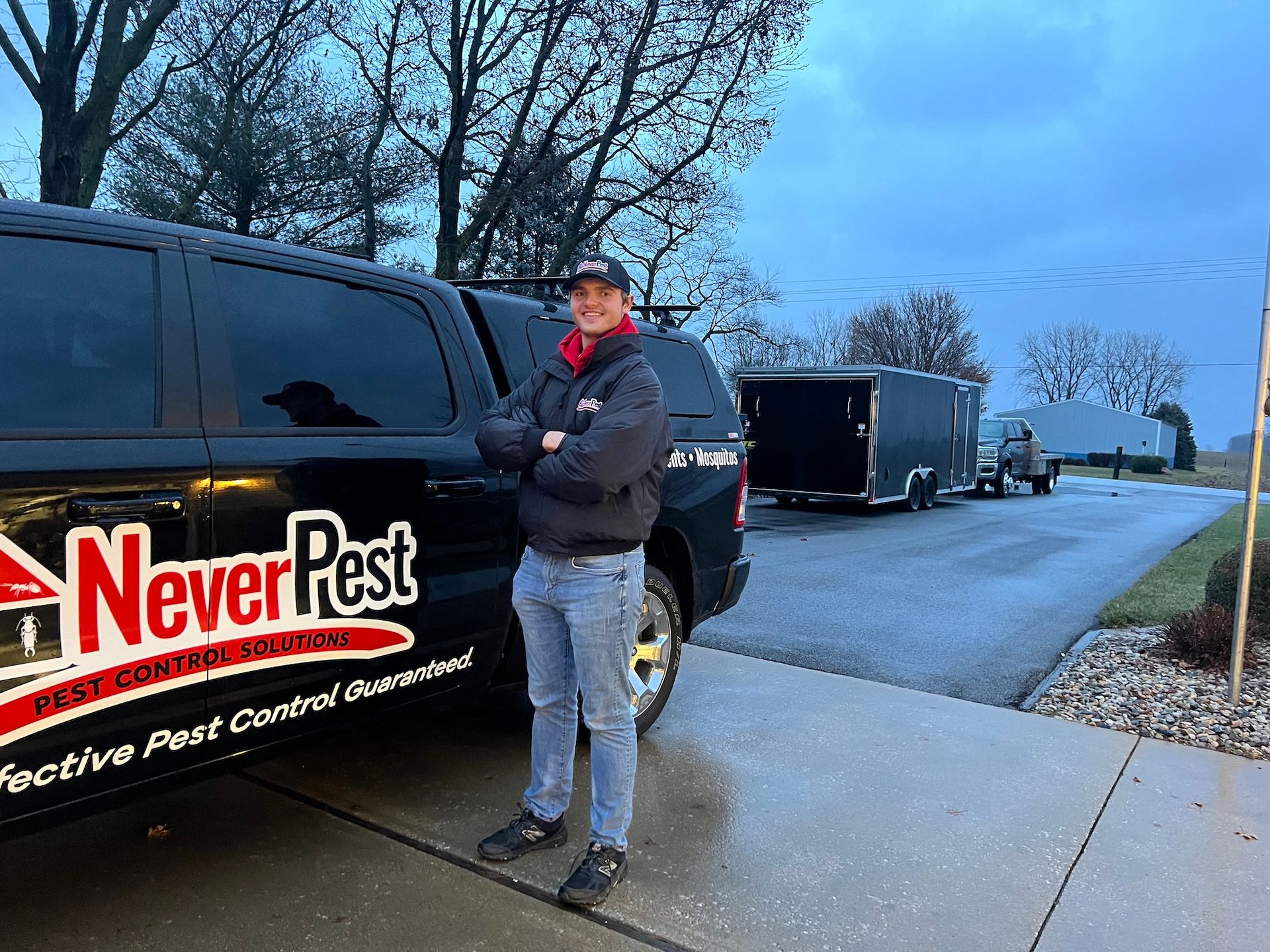 Person standing beside a black Never Pest service truck in a driveway at dusk