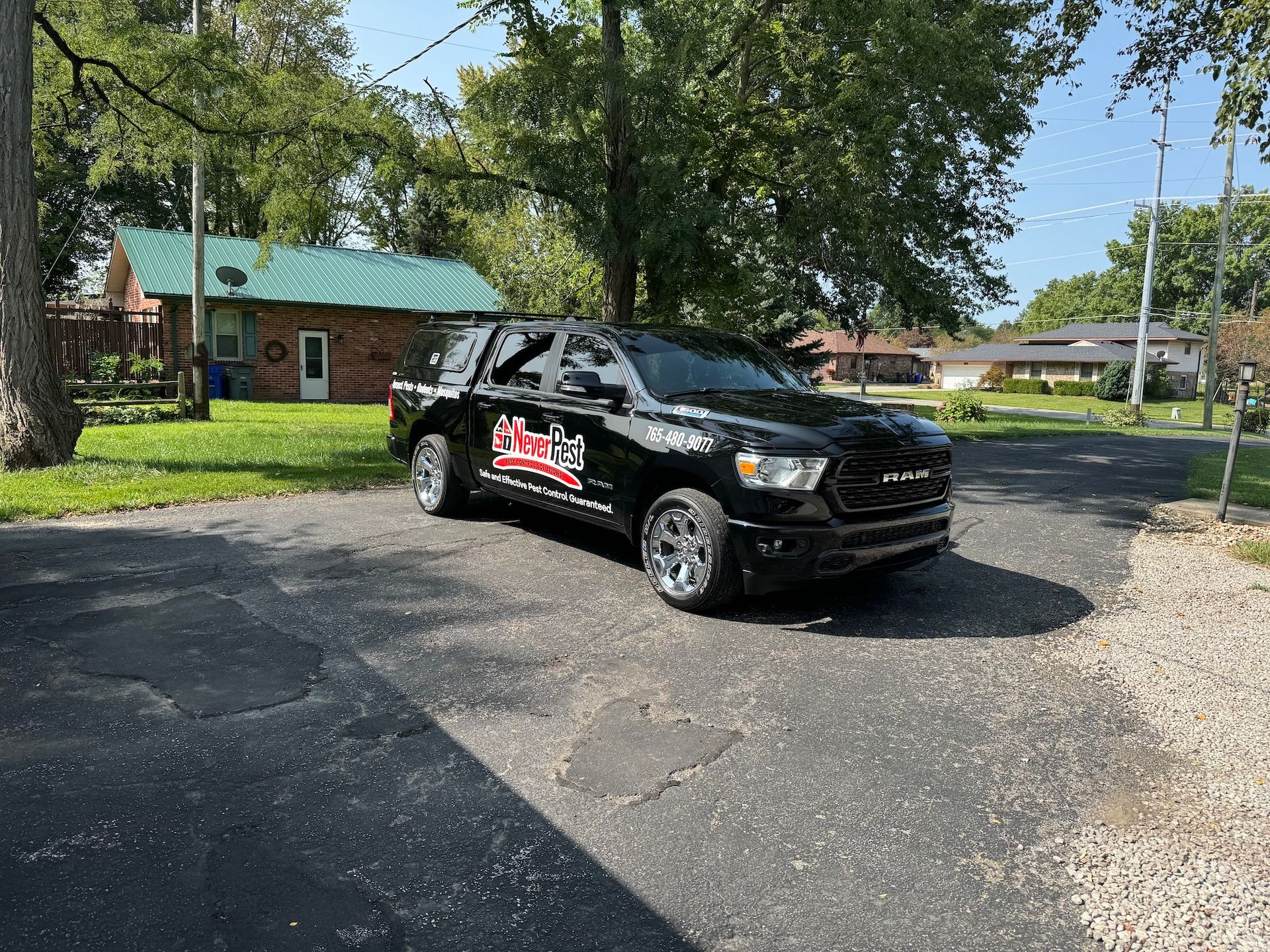 Black SUV with red logo parked on a gravel driveway beside a house and trees.