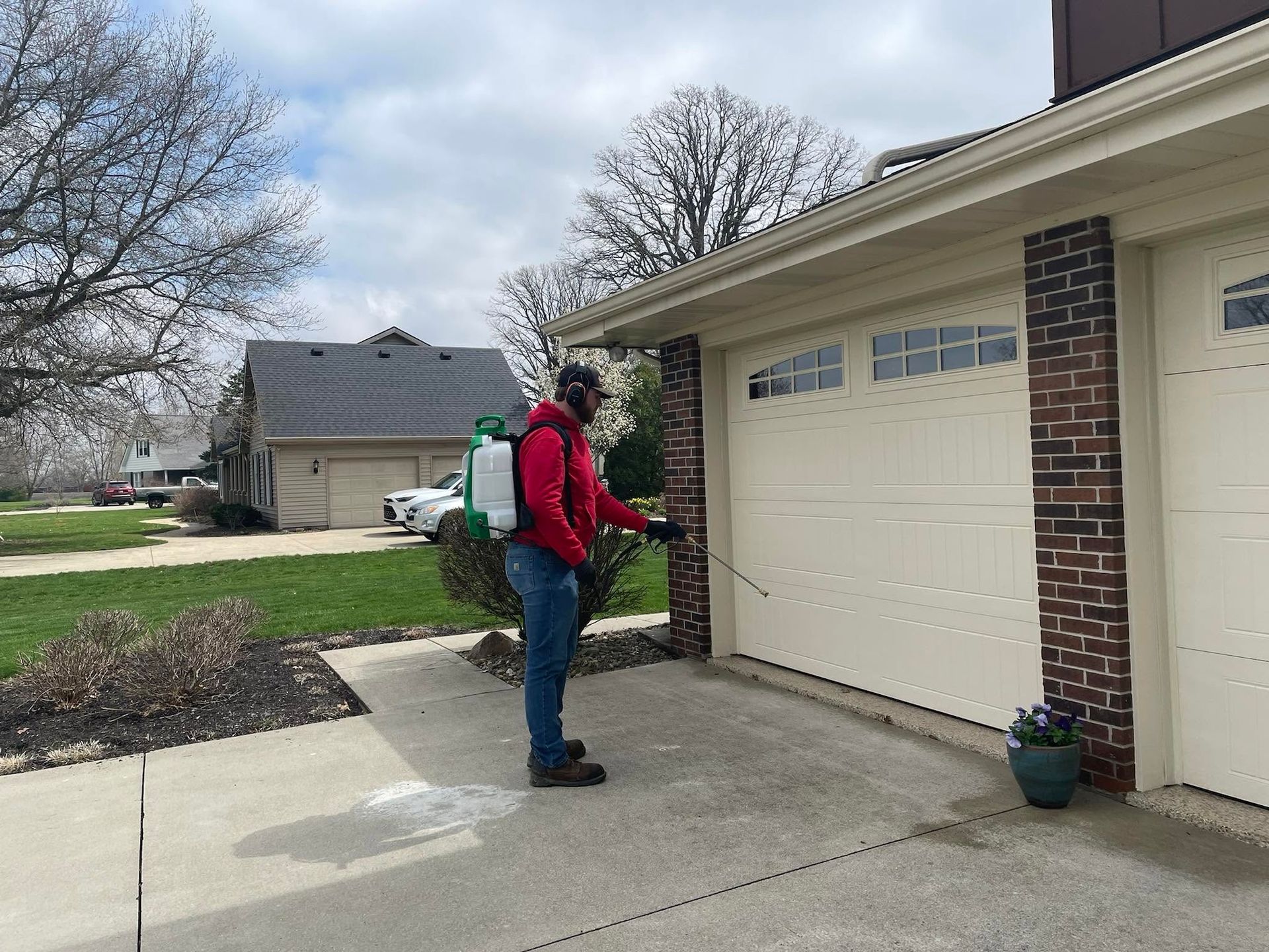 Person in red backpack stands by a garage door, spraying or inspecting the driveway.