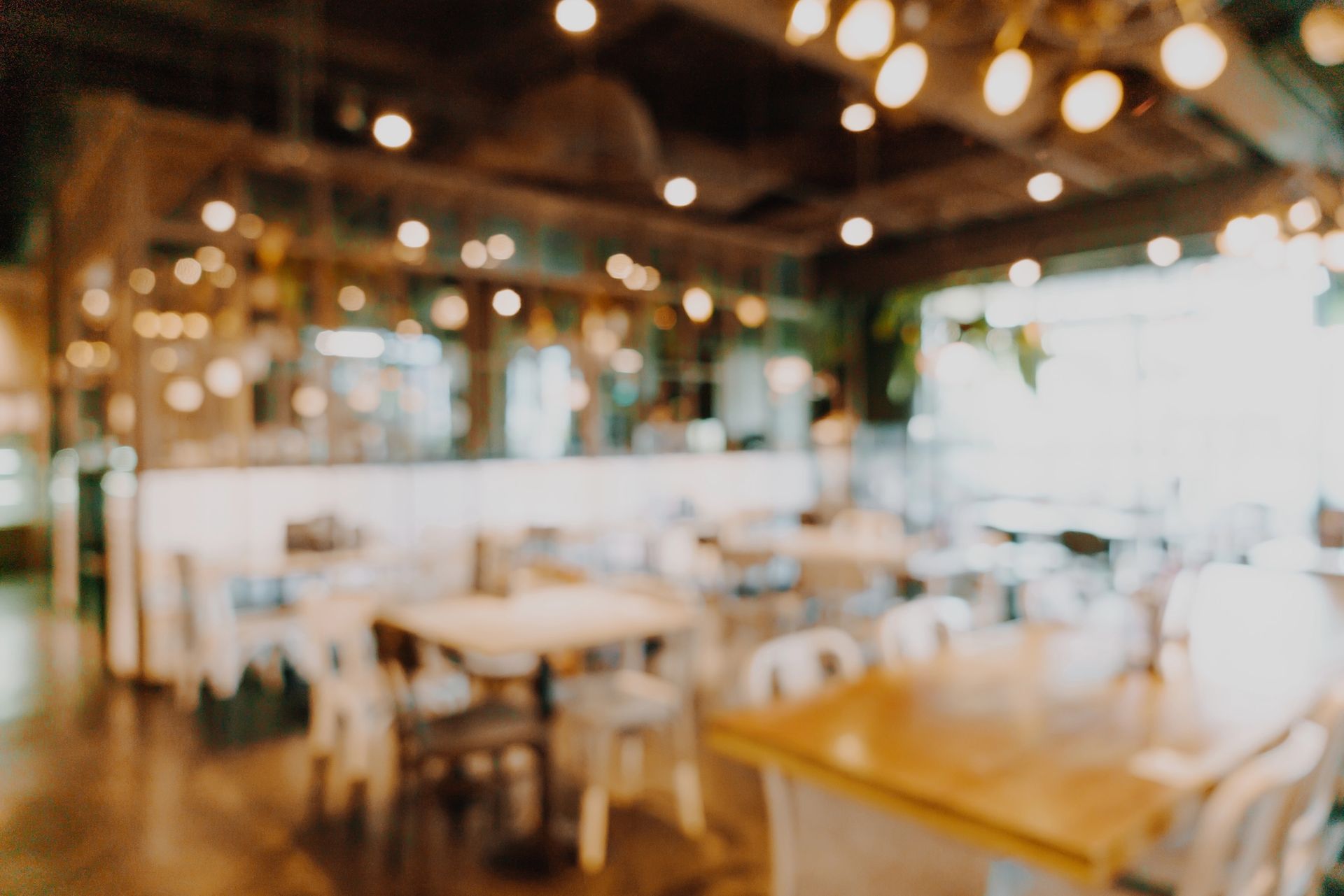 Blurred bright cafe interior with wooden tables, chairs, and hanging lights