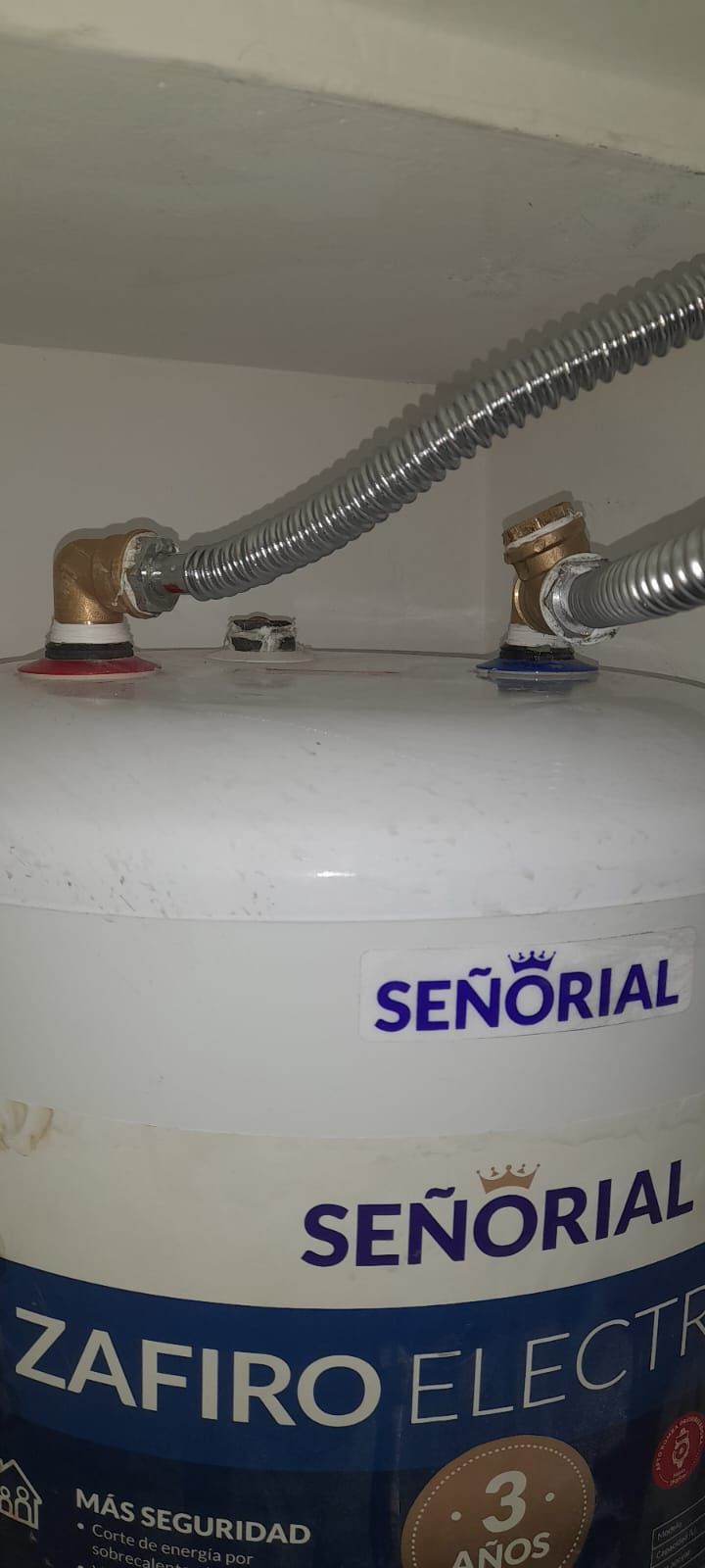 Tanque de calentador de agua blanco con mangueras plateadas y etiqueta azul SEÑORIAL ZAFIRO ELECTRIC.