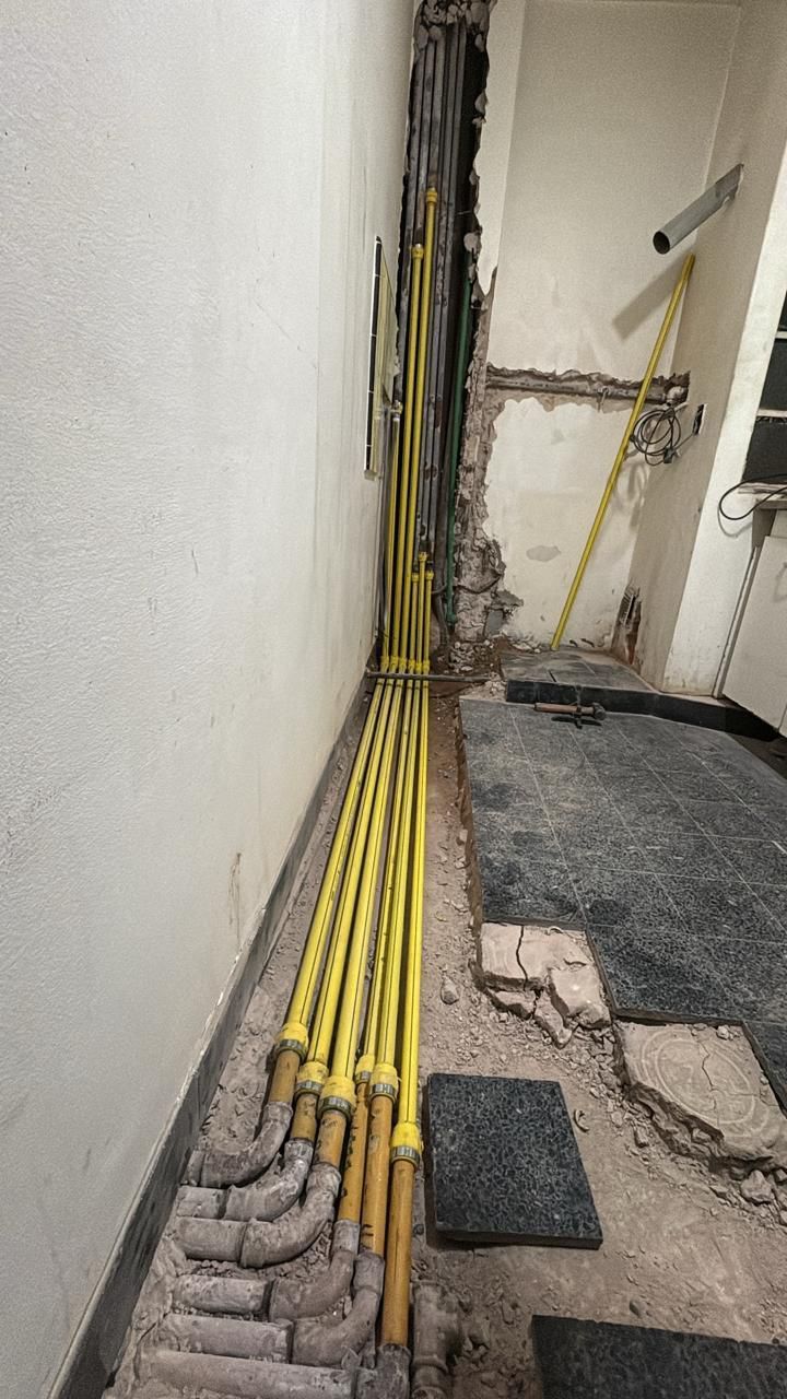 En un pasillo estrecho y sin terminar, con cables expuestos y escombros, se ven tuberías amarillas de servicios públicos que discurren a lo largo de una pared.
