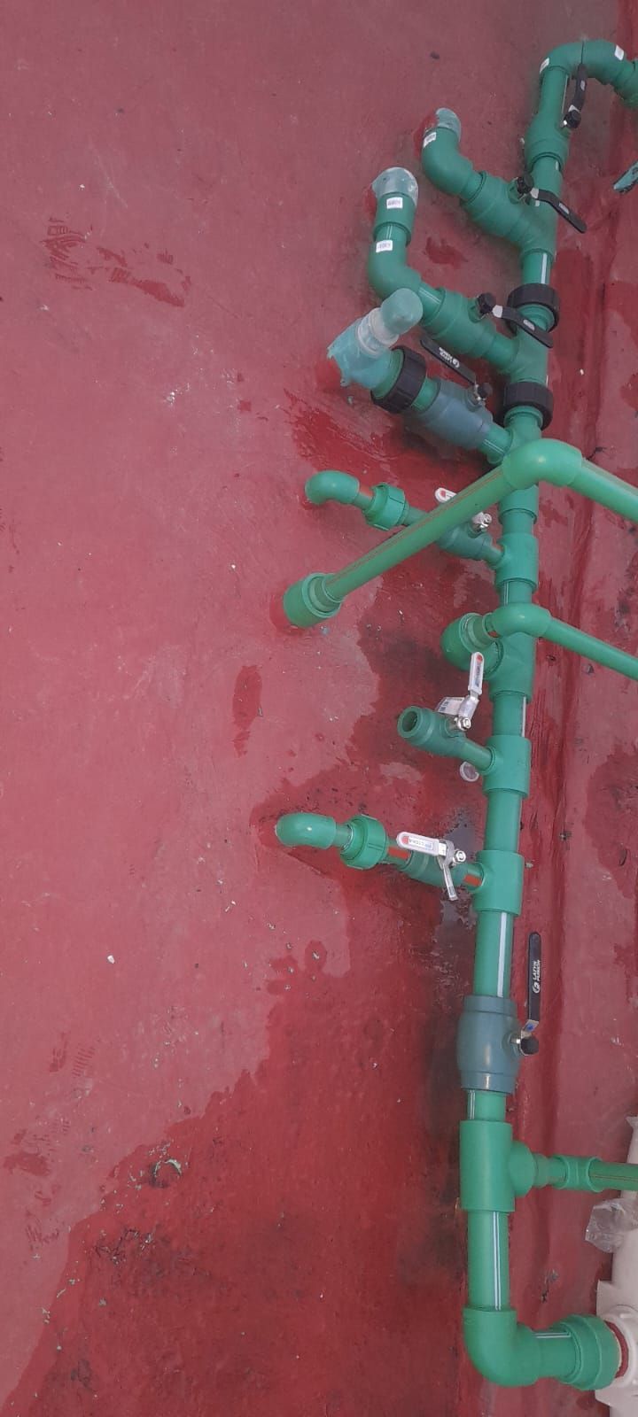 Tuberías y válvulas de riego de color verde montadas en una pared roja.