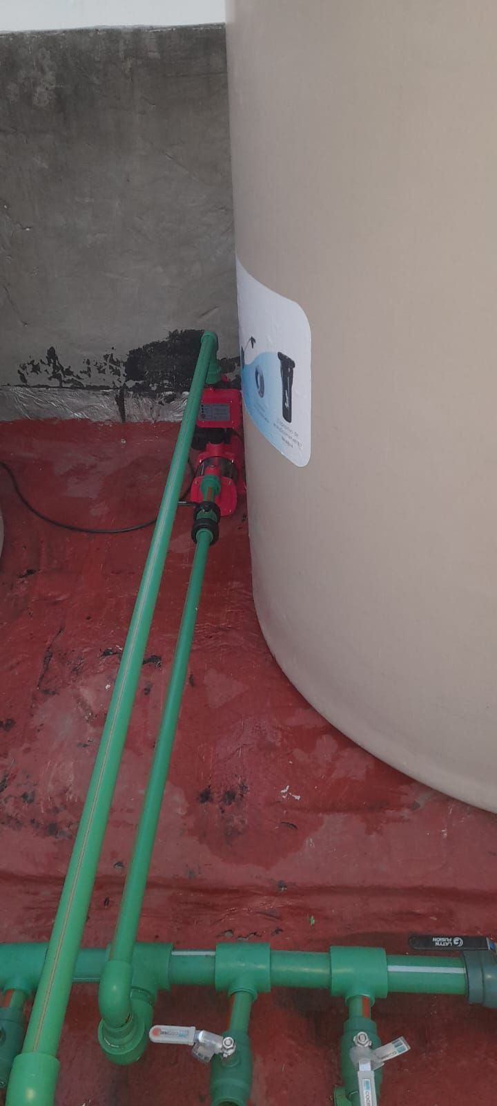 Tuberías verdes conectadas a un tanque cilíndrico de color beige sobre un suelo rojo en el interior.