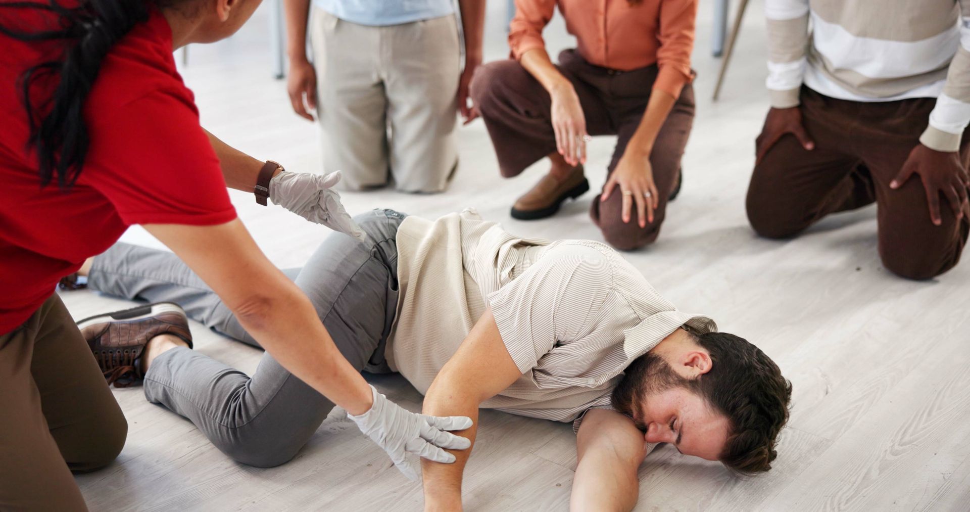 Person lying on the floor during a group CPR training session, with others kneeling nearby