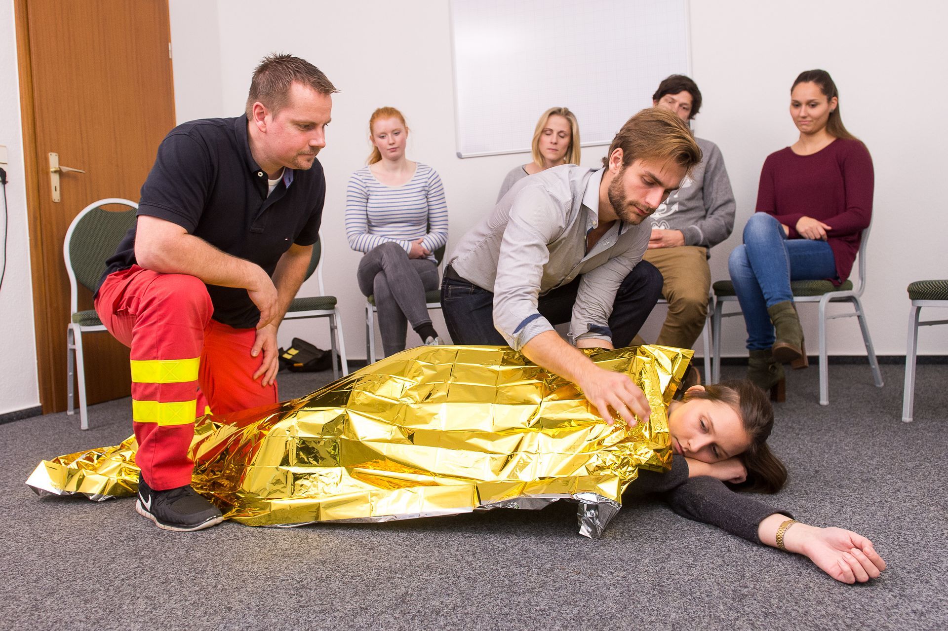 Rescue training scene with a person wrapped in a gold thermal blanket while responders assist nearby