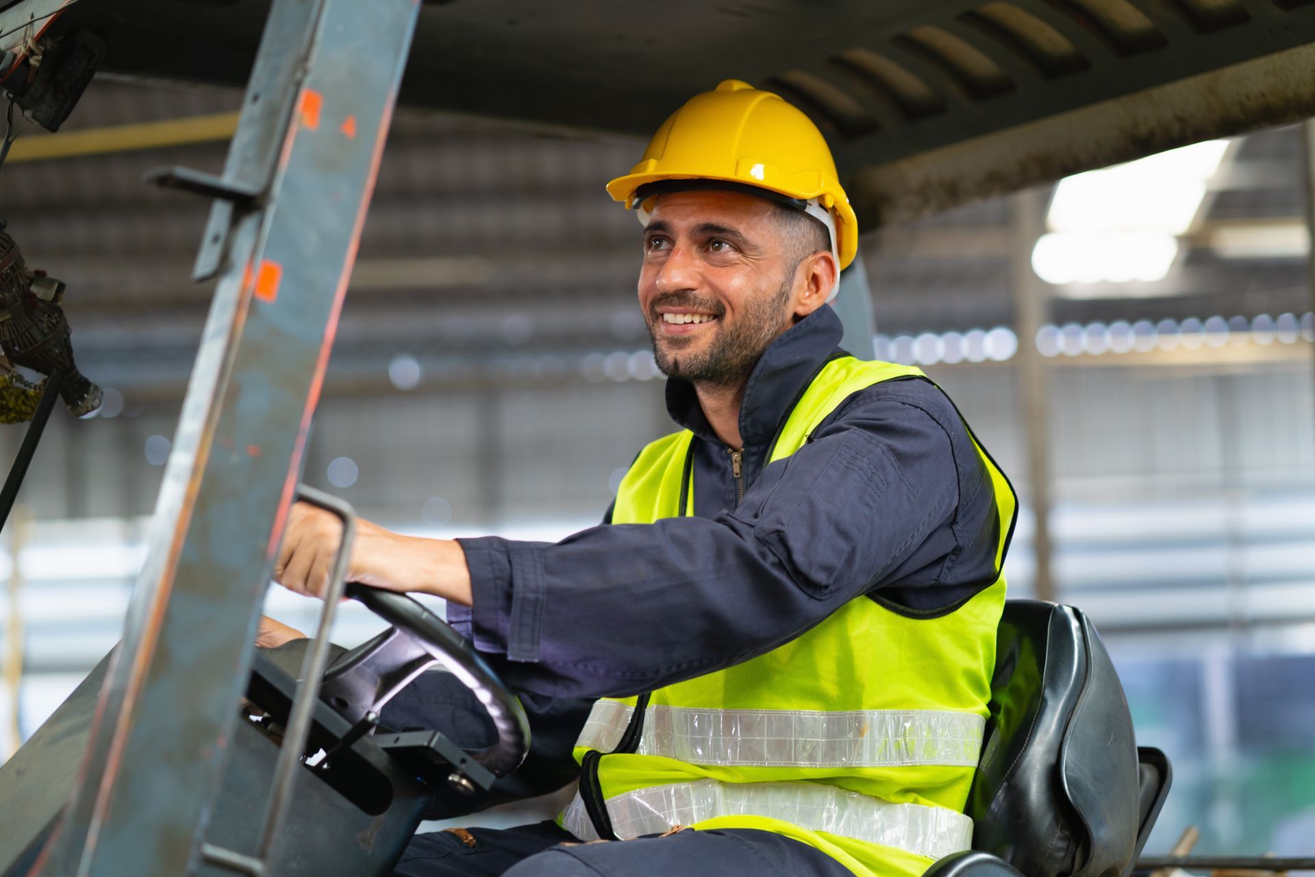Worker in a yellow hard hat and safety vest driving a forklift in a warehouse