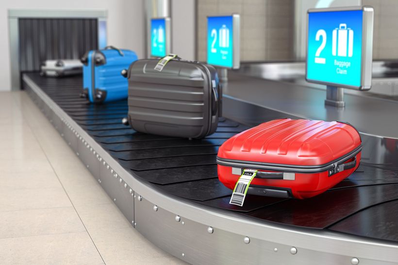 A red suitcase is on a conveyor belt at an airport.