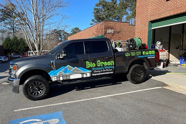Black Big Green pickup truck parked outside a brick building with garage doors and a sunny street backdrop