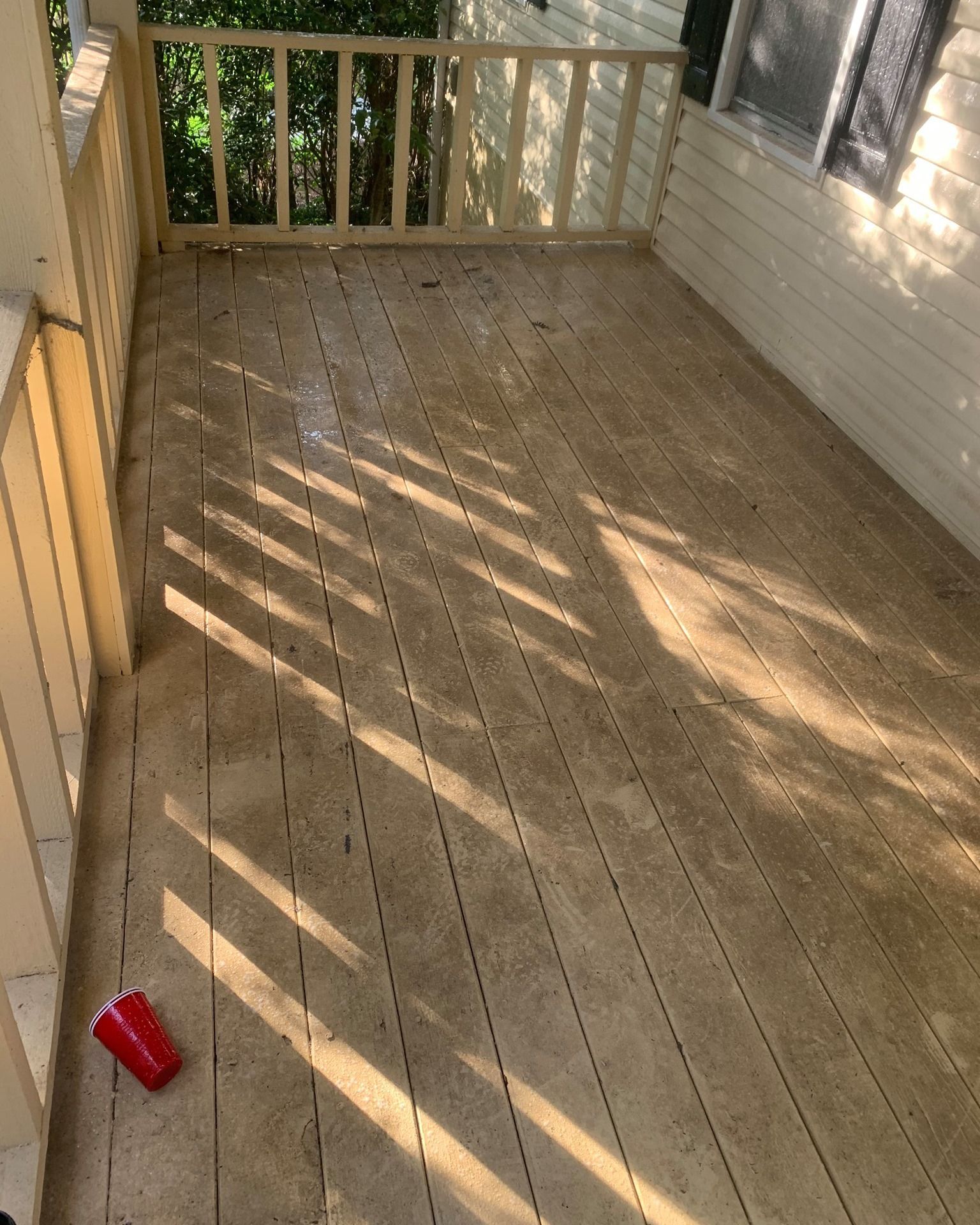 Wooden porch deck with railing, sunlit shadows, and a red cup on the floor.