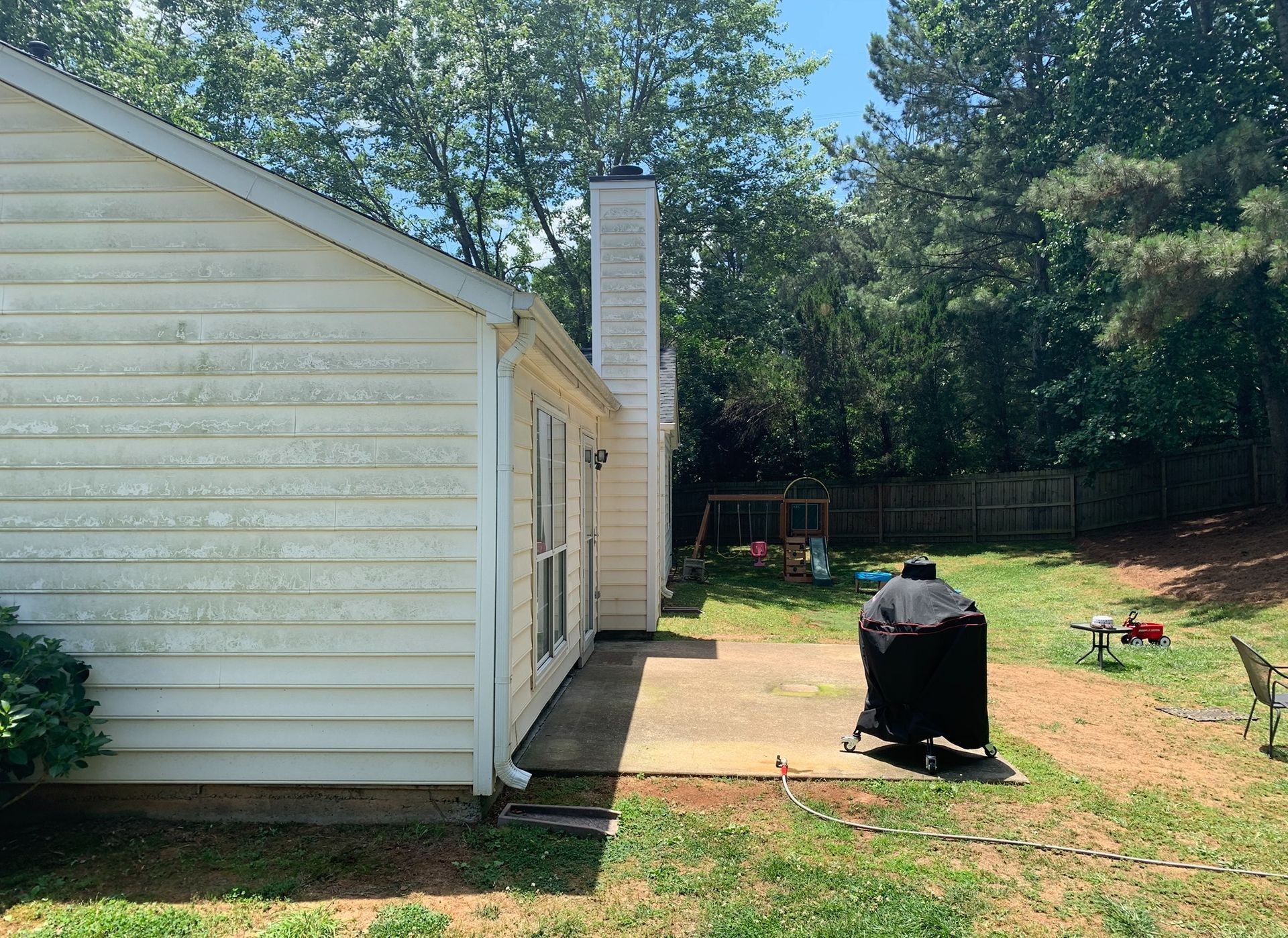Backyard beside a white house with a patio grill and trees in the background
