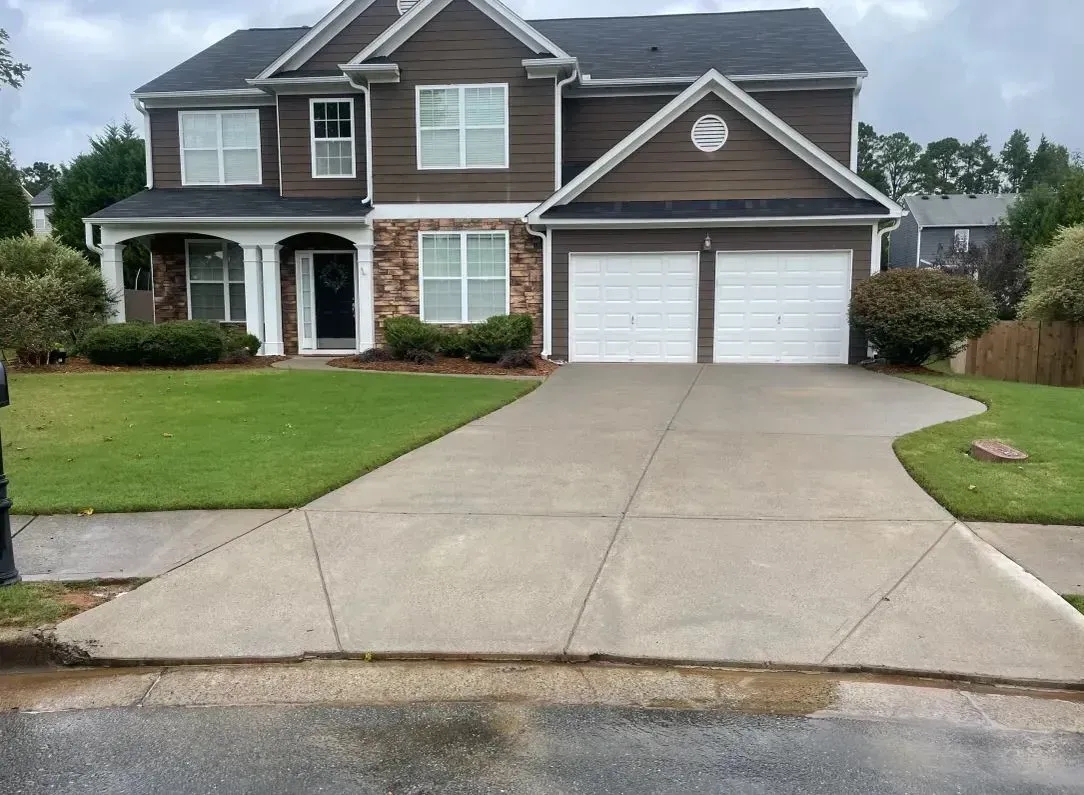 Two-story suburban brick house with a two-car garage and large driveway on a green lawn