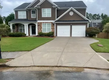 Two-story suburban house with a double garage and wide concrete driveway, front lawn and shrubs.