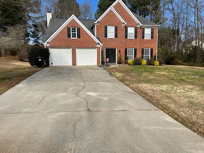 Brick two-story house with two-car garage and long concrete driveway under a clear sky