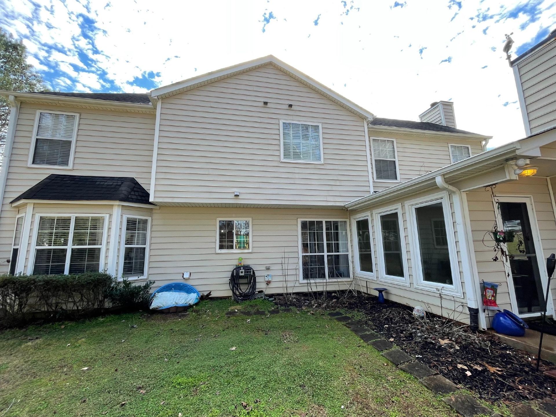Suburban two-story house with light siding, covered porch, and small front yard under a cloudy sky