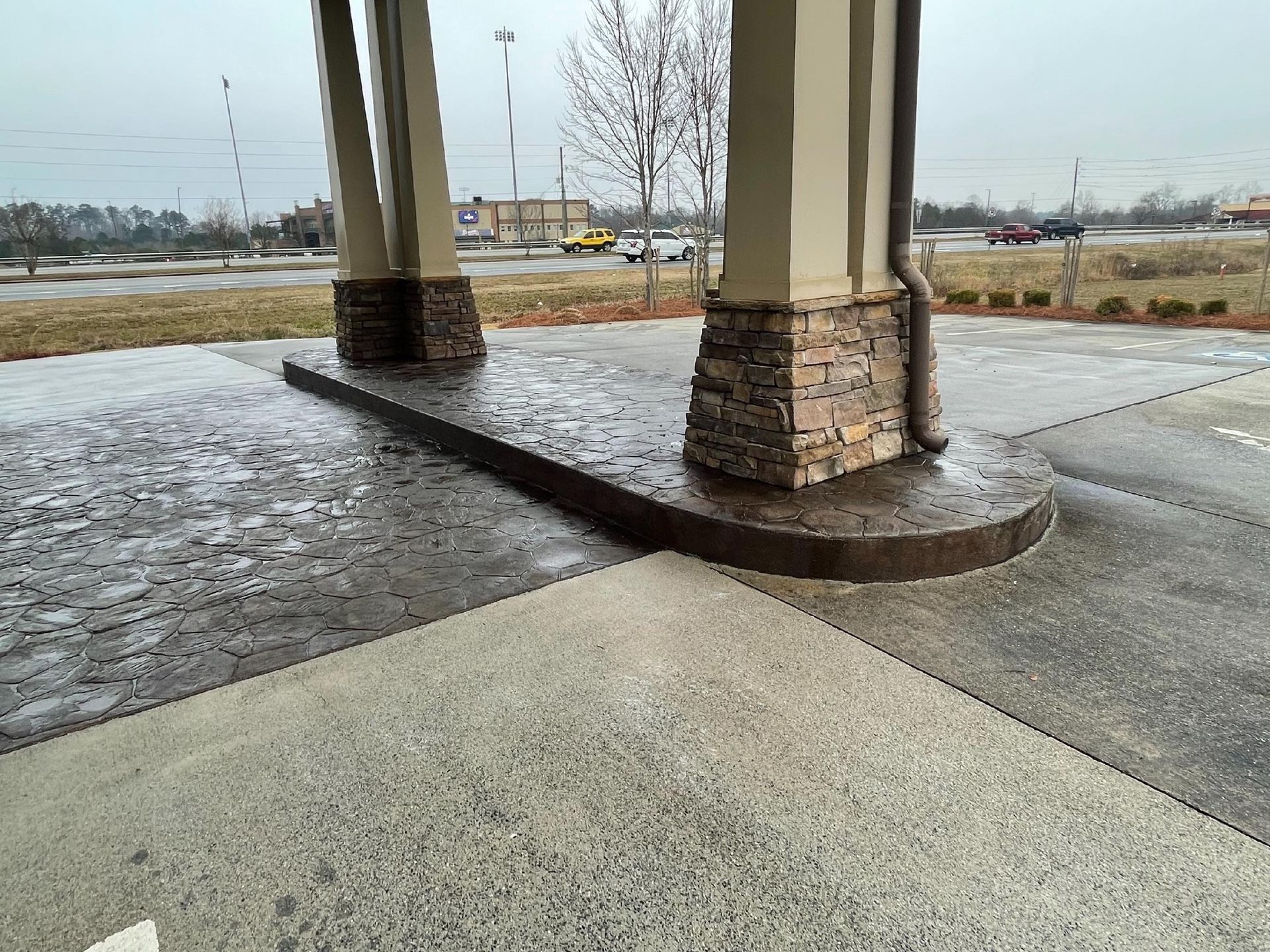 Snow-dusted concrete under a covered structure with stone-clad columns on a cloudy day