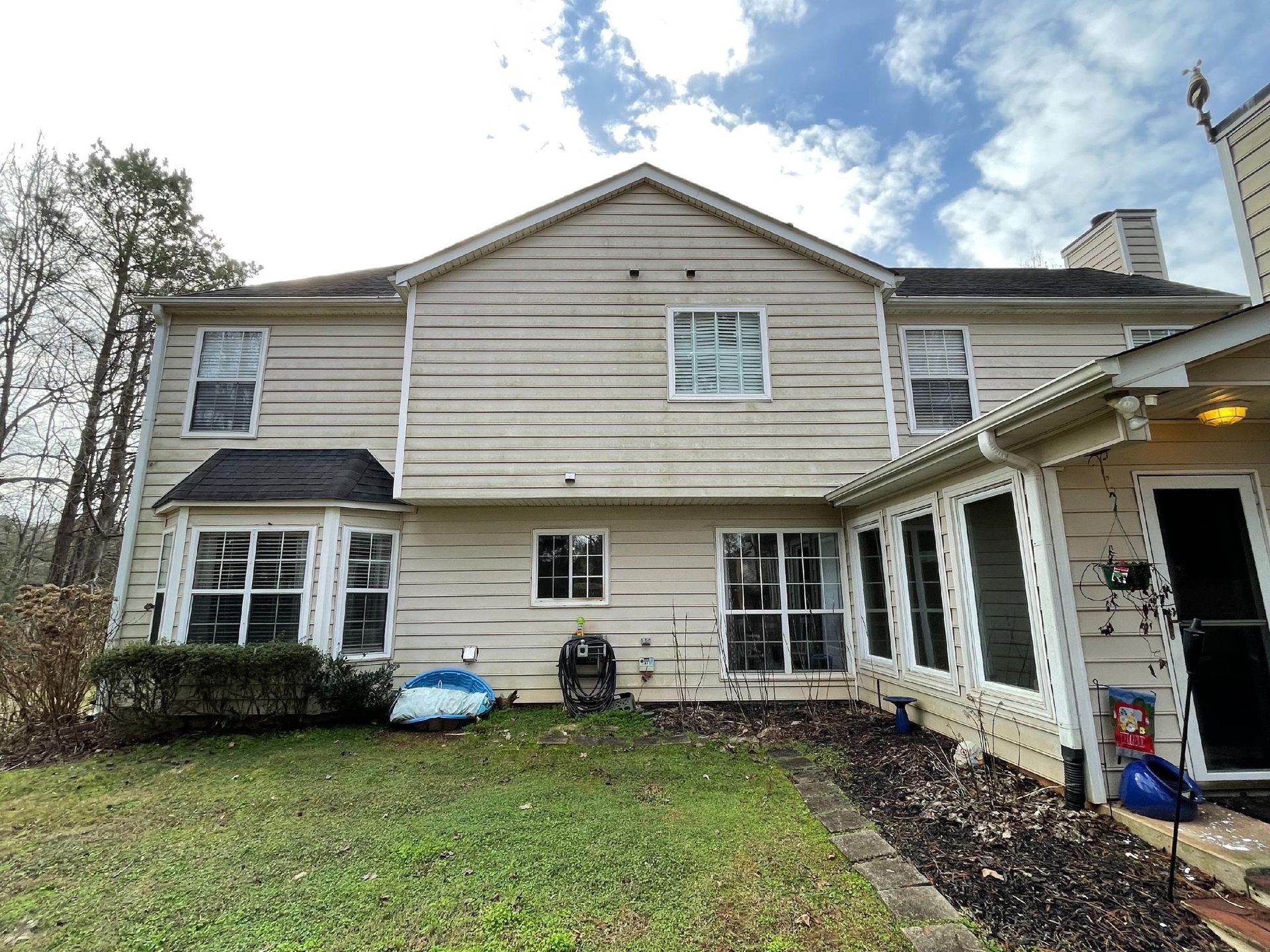 Two-story beige house with white trim and a covered porch, seen from the backyard.