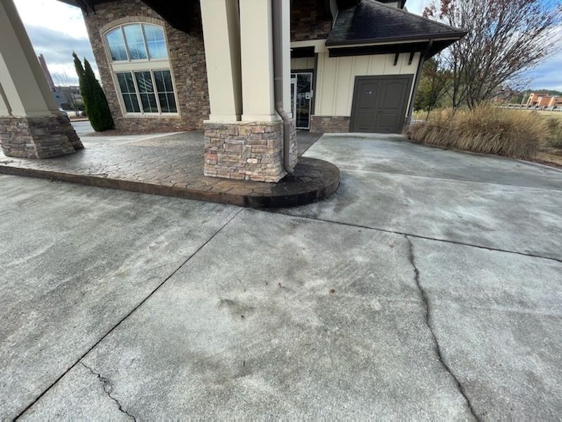 Cracked concrete driveway beside a house with stone columns and a garage door